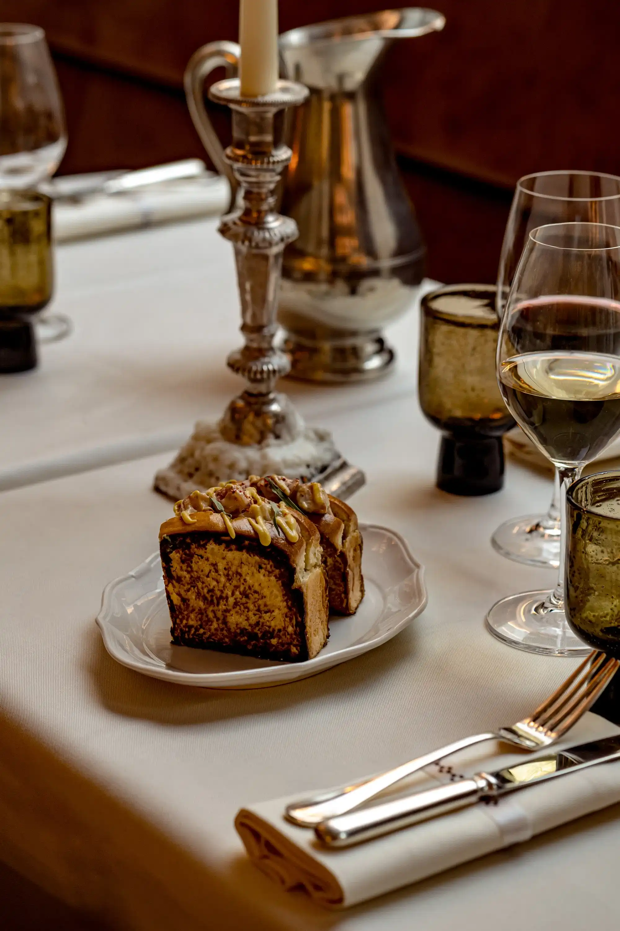 Due fette di torta su un piatto bianco su un tavolo con bicchieri da vino e posate in un ristorante.