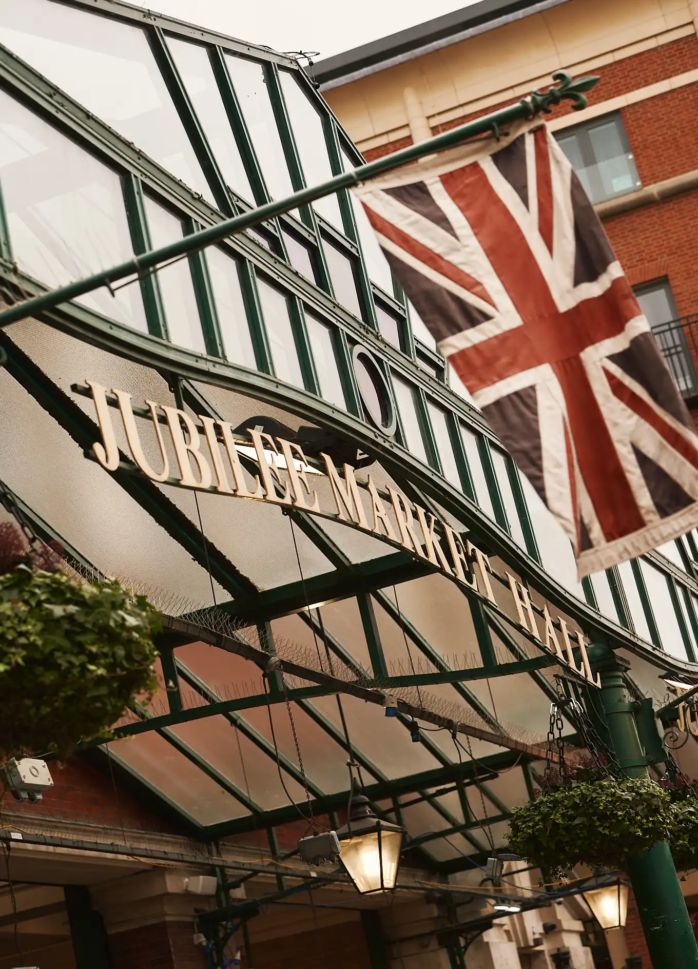 Bandiera Union Jack appesa all'esterno del Jubilee Market Hall con ingresso in metallo verde e vetro.