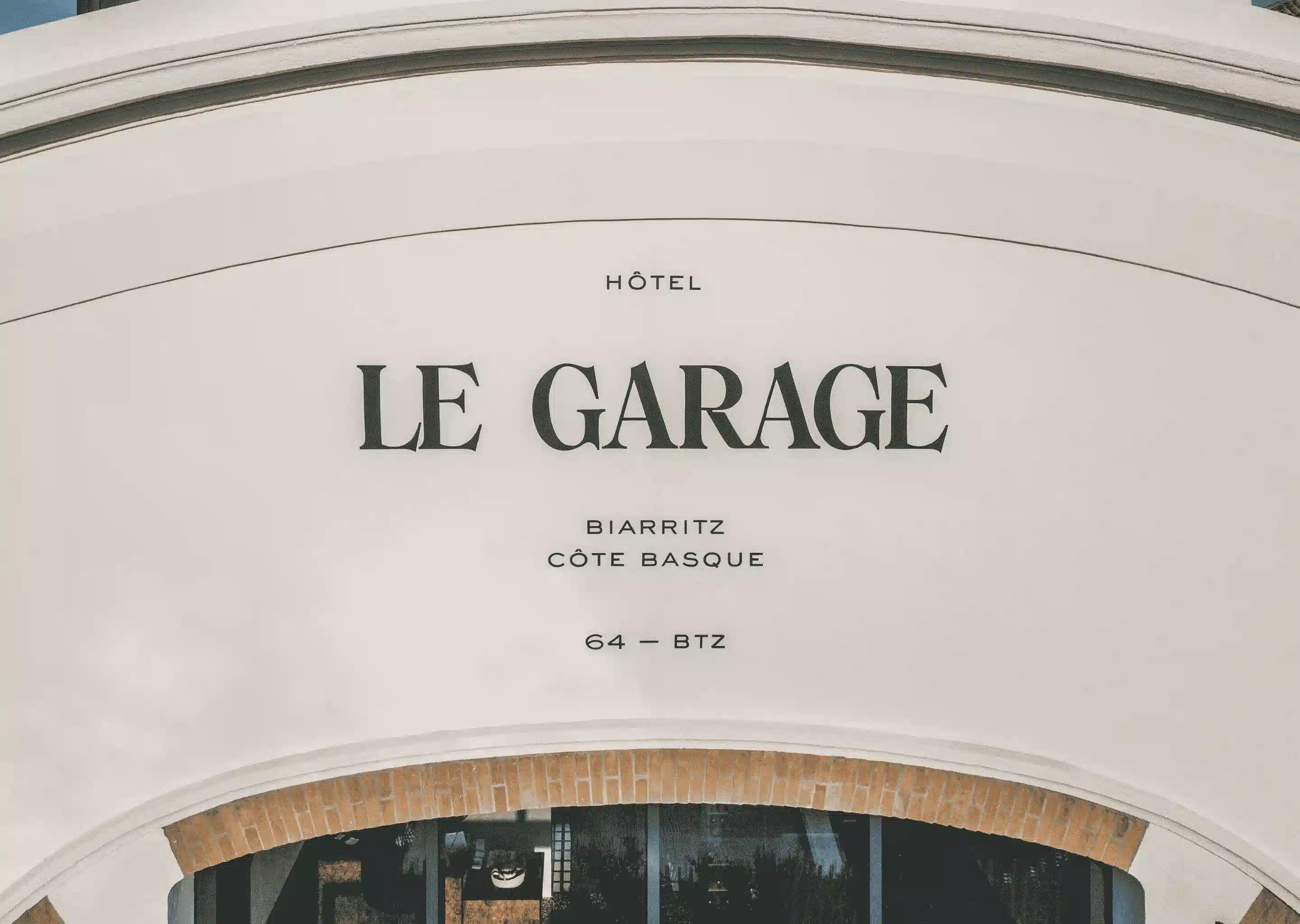 Insegna dell'Hotel Le Garage su una parete ad arco bianca sopra un ingresso con cornice in mattoni.