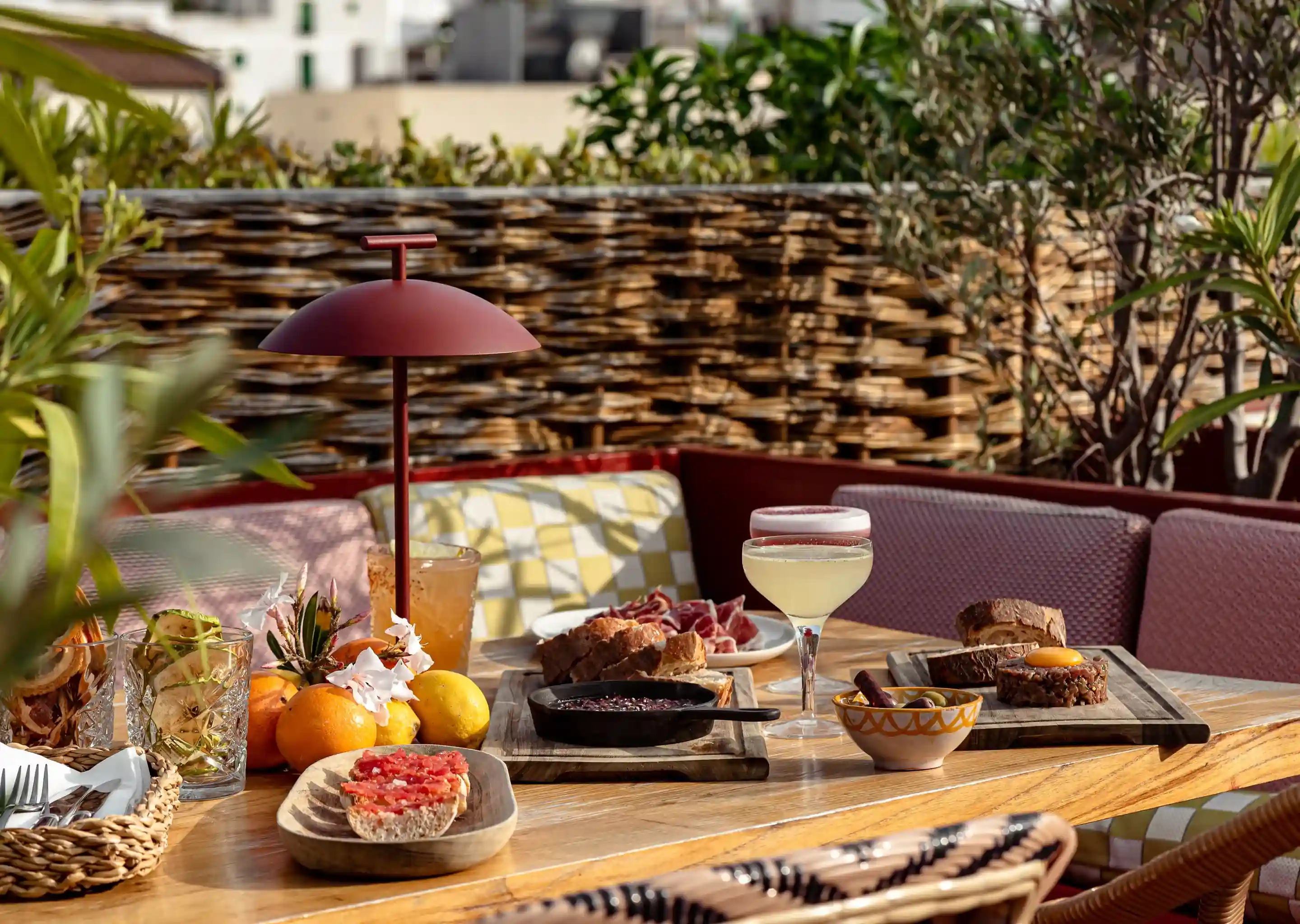 Mesa ao ar livre com bebidas, pão, frutas, charcutaria e pequenos pratos em um ambiente aconchegante de pátio.