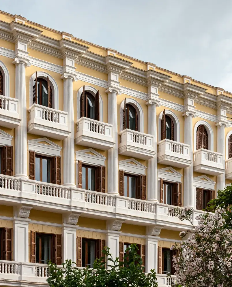 Fachada de edifício clássico em amarelo e branco com varandas e janelas com persianas de madeira.