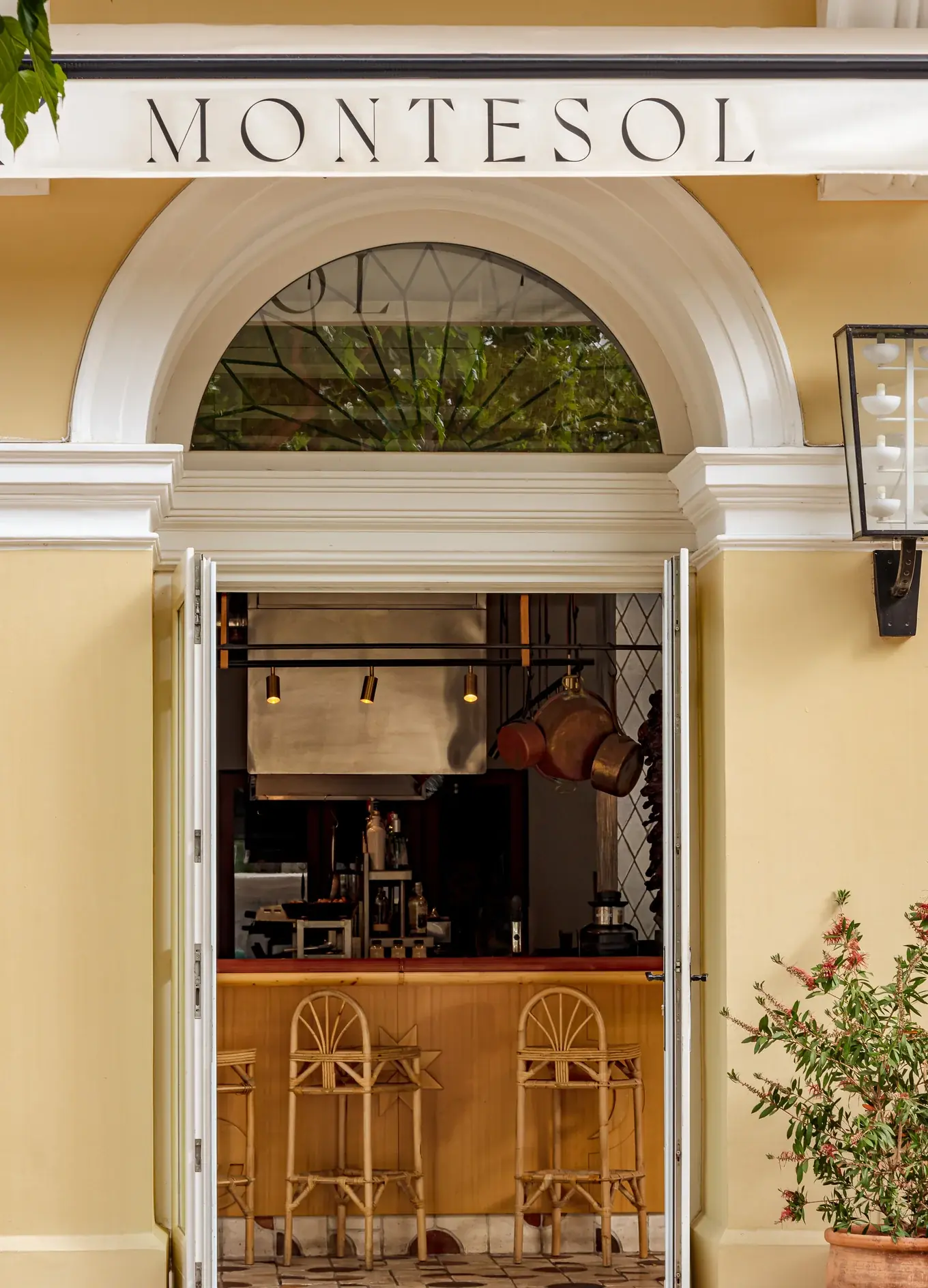 Entrada aberta para Montesol com bancos de bar de madeira e vasos pendurados dentro de um café aconchegante.