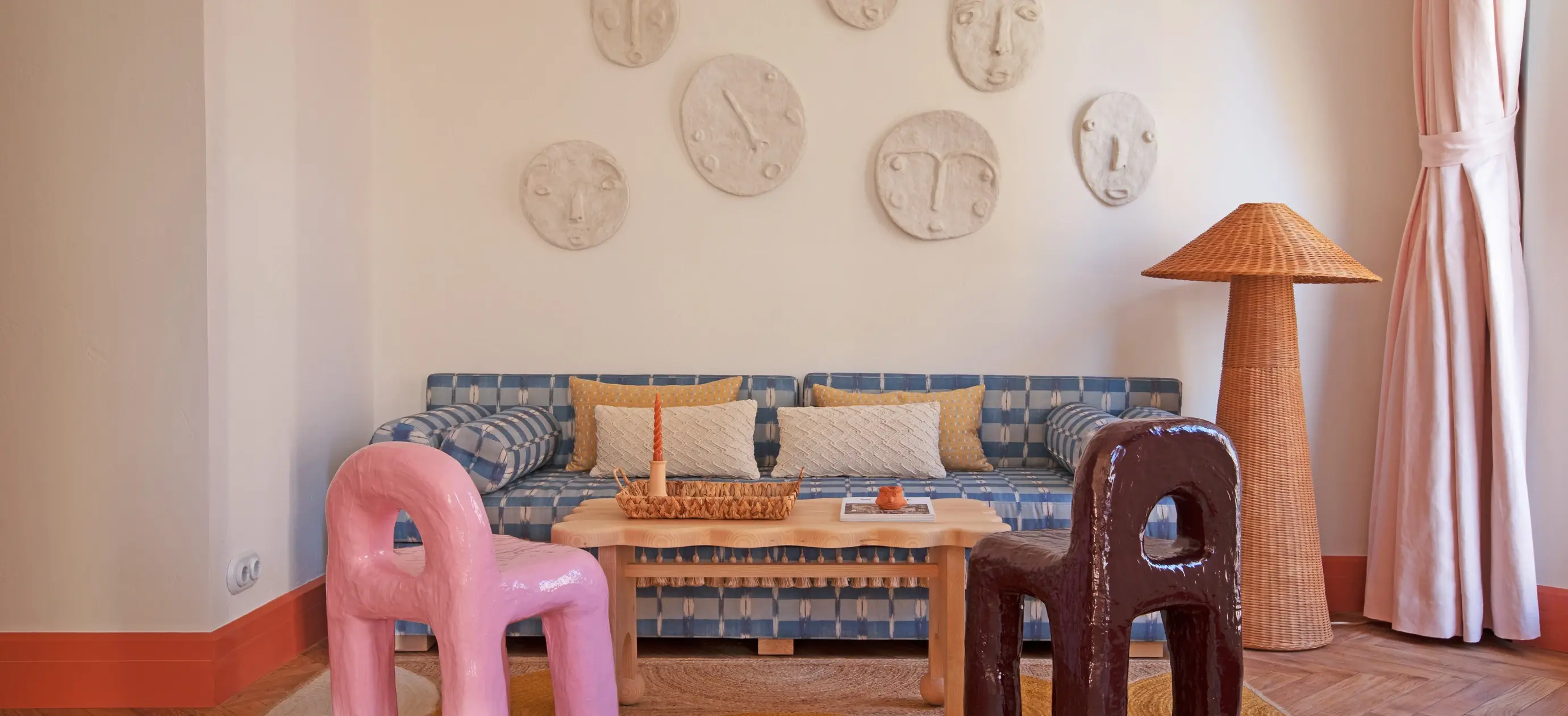 Aconchegante sala de estar com sofá xadrez azul, duas cadeiras artísticas, mesa de madeira e máscaras de parede.