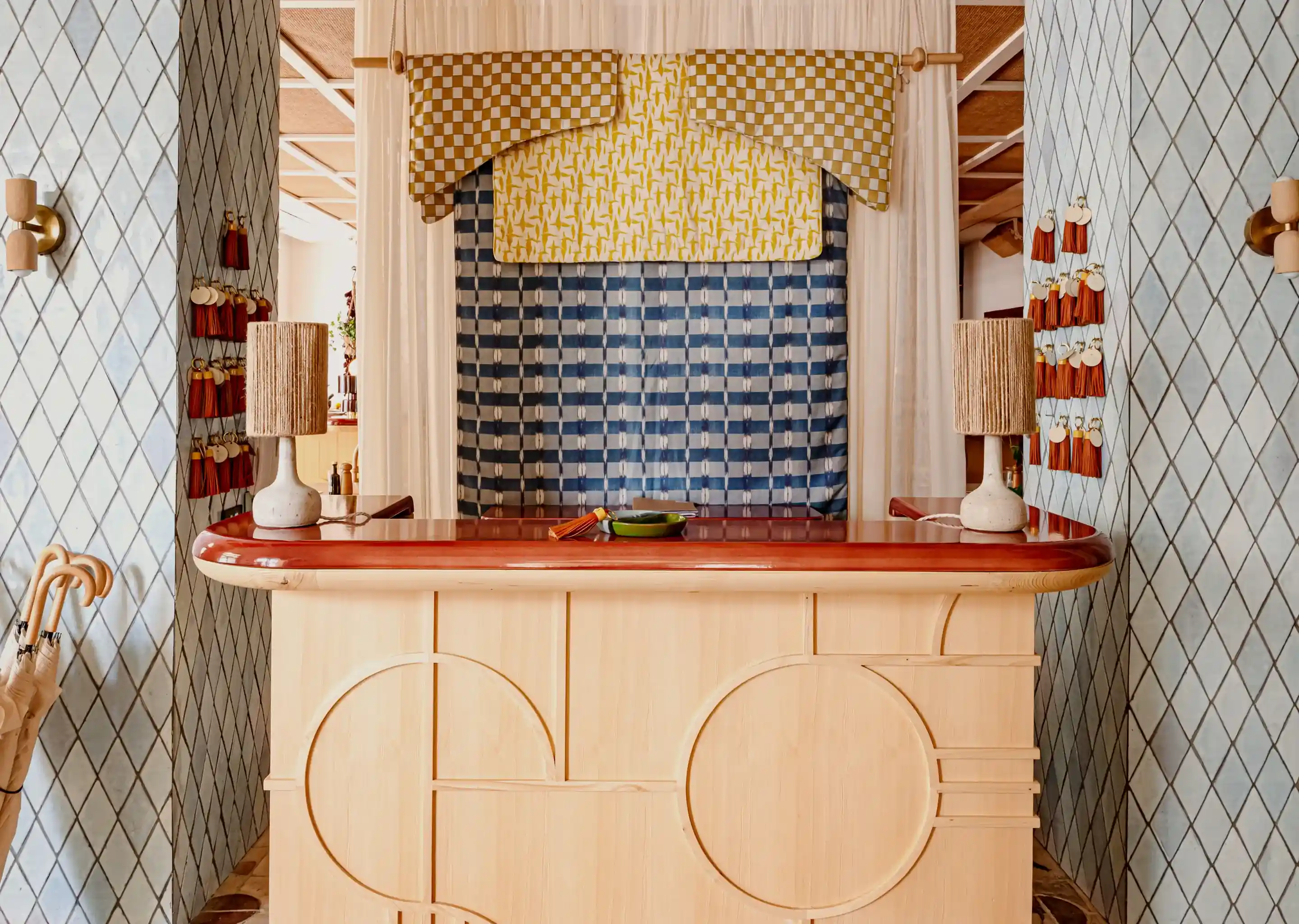 Balcão de recepção do hotel com pano de fundo estampado, luminárias, guarda-chuvas e chaveiros pendurados em paredes de azulejos.