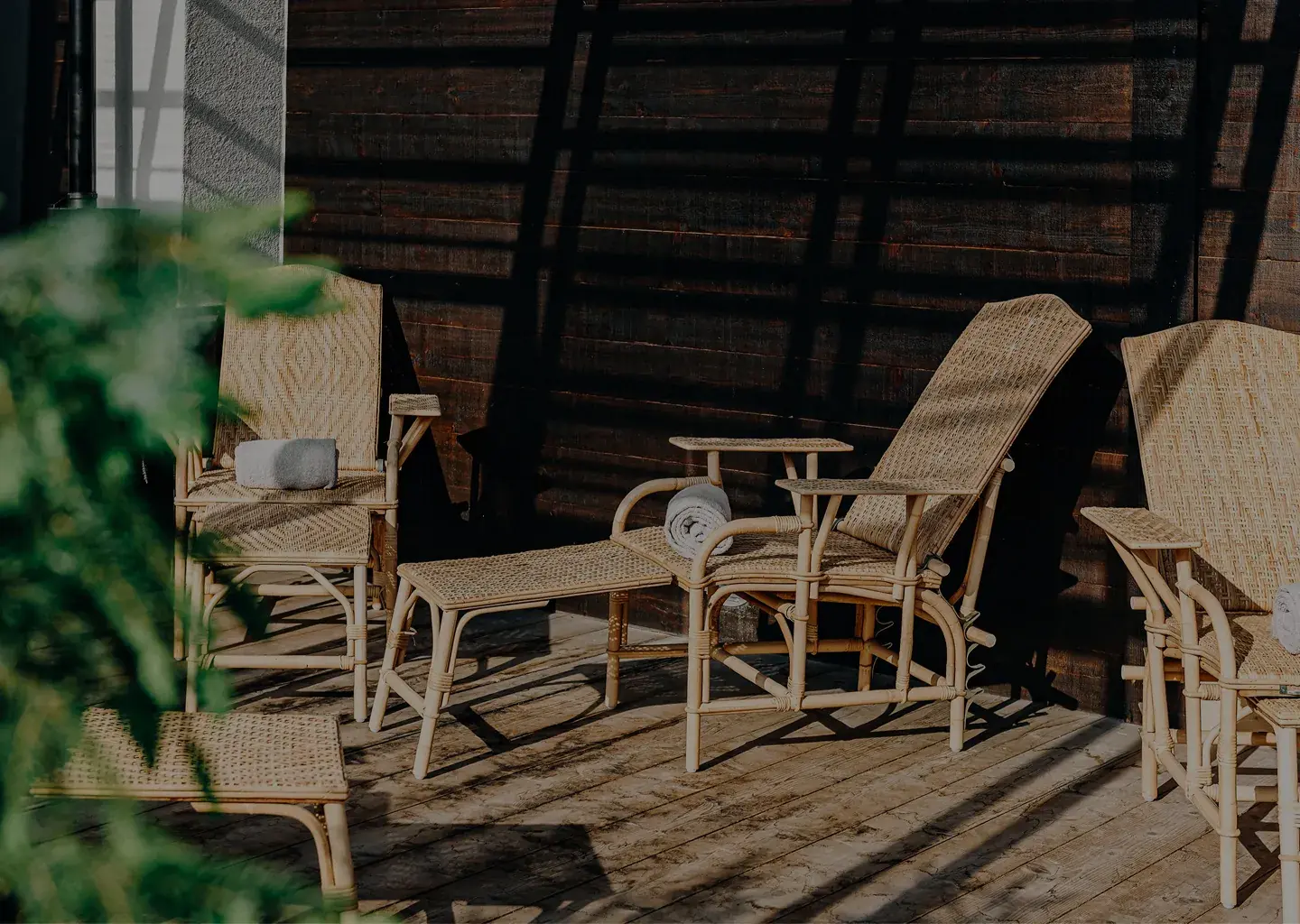 Cadeiras e espreguiçadeiras de vime ao ar livre em deck de madeira com toalhas enroladas na luz do sol e nas sombras.
