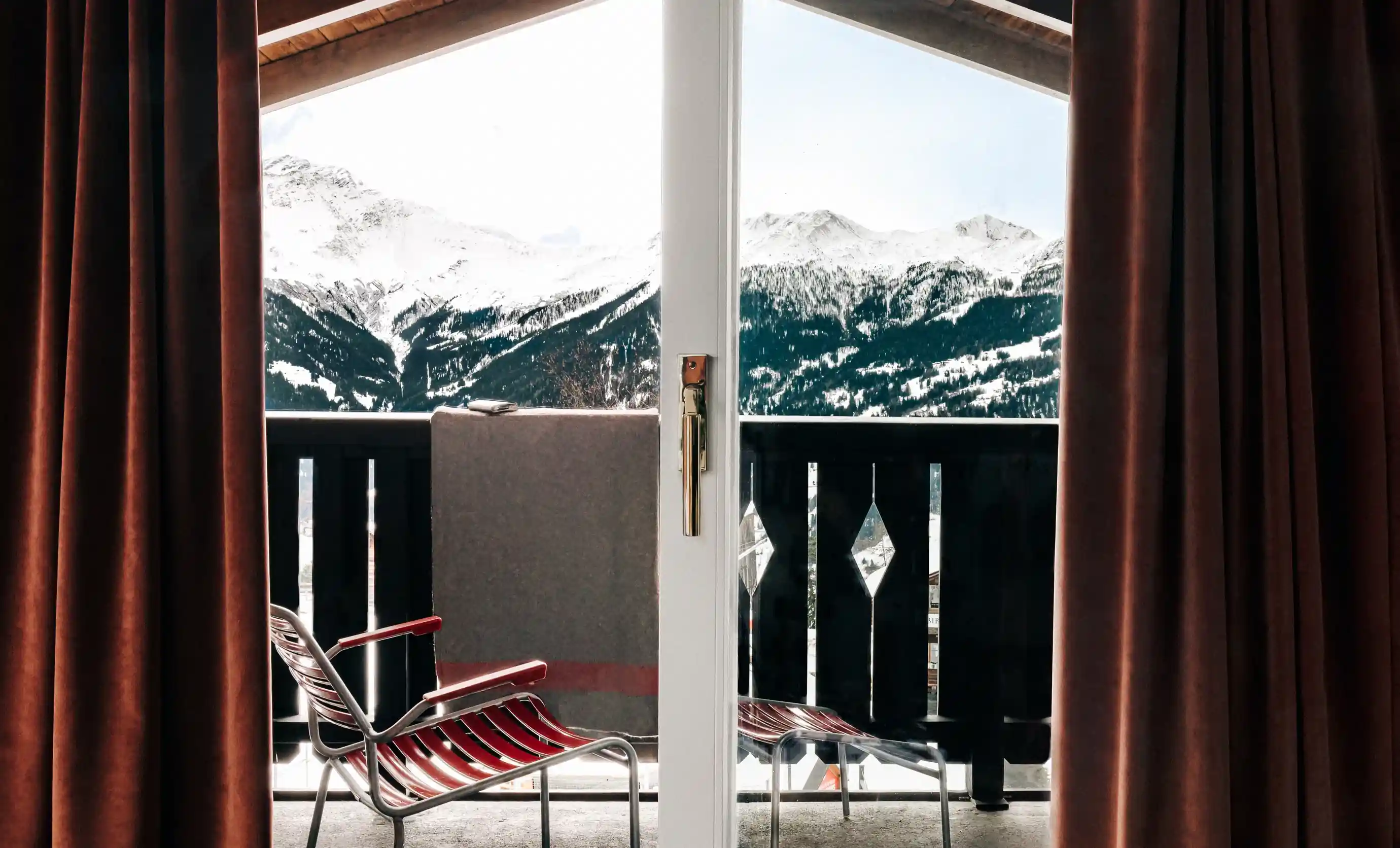 Vista da varanda de um quarto com duas cadeiras e picos de montanhas nevadas ao fundo.