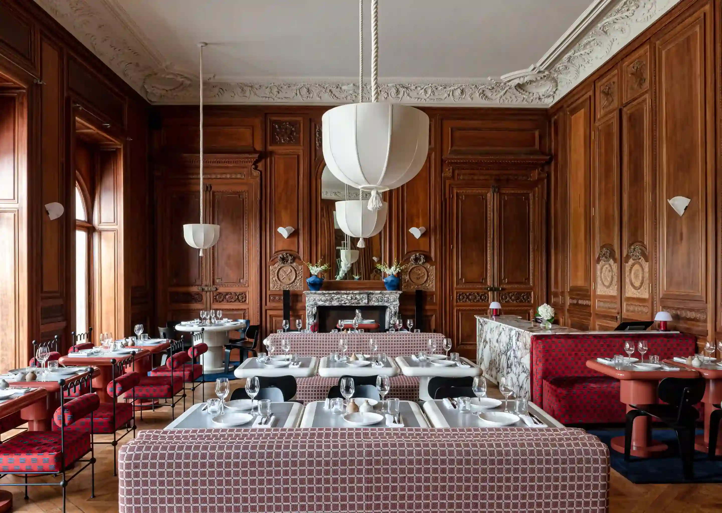 Elegante sala de jantar com paredes de painéis de madeira, assentos estampados, mesas brancas e luminárias pendentes brancas suspensas.