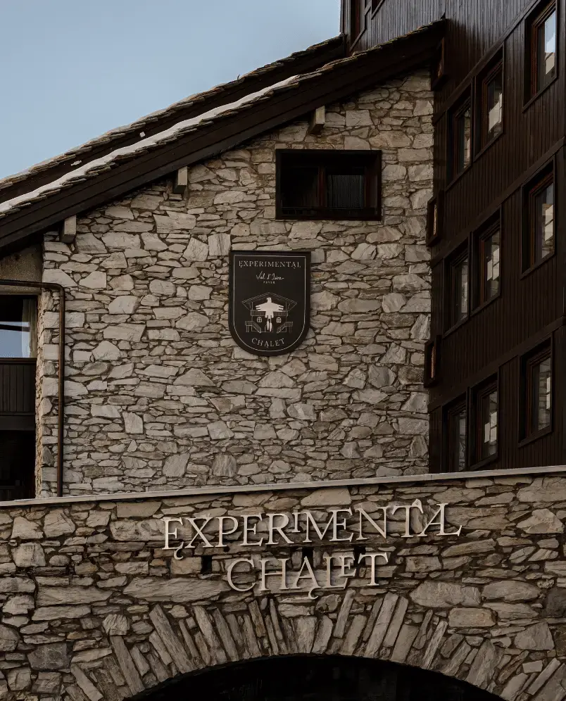 Esterno in pietra di un edificio con un cartello con la scritta «EXPERIMENTAL CHALET» e uno scudo con il logo sopra.
