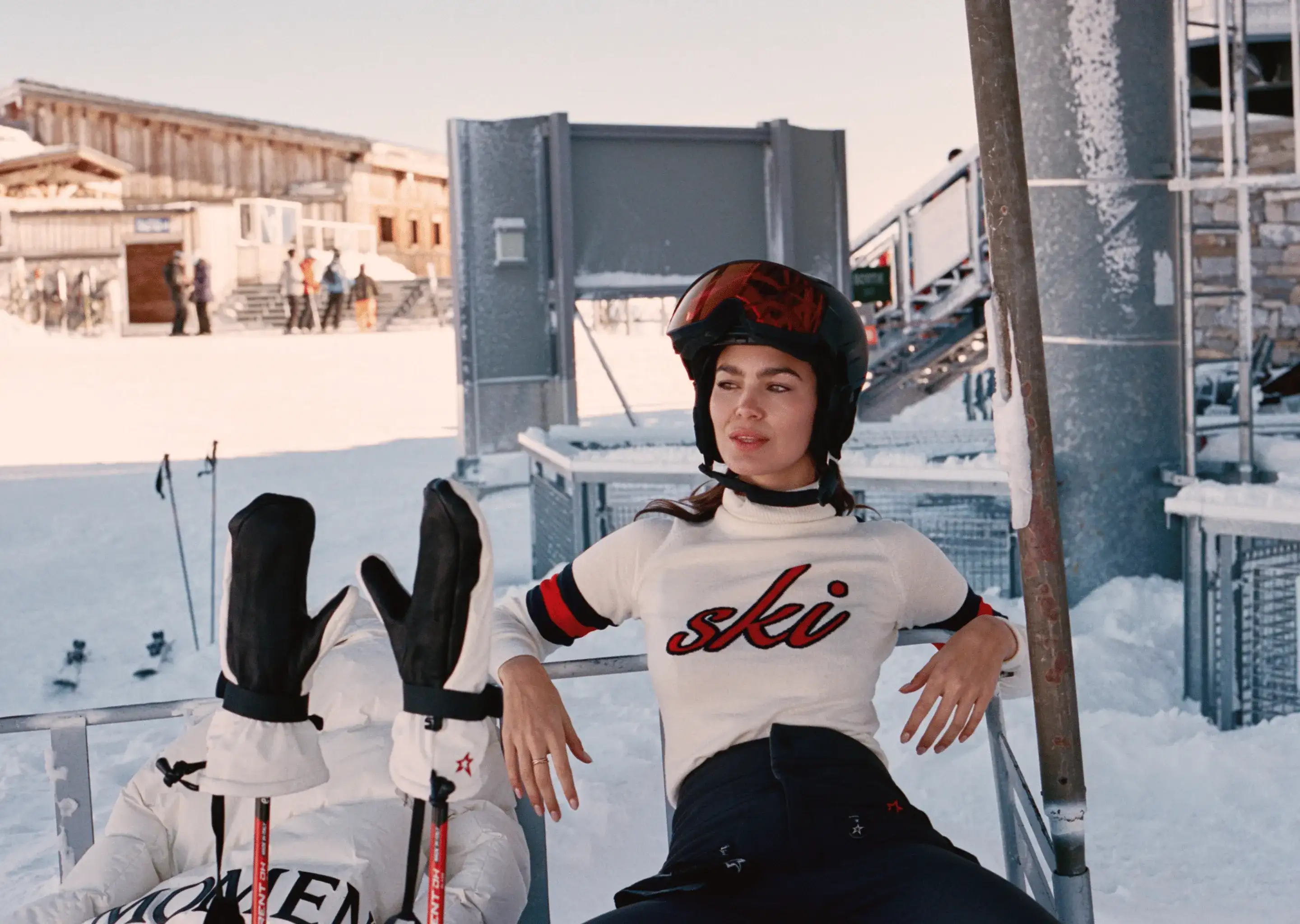 Donna con casco da sci e maglione seduta su un impianto di risalita in una stazione sciistica innevata.