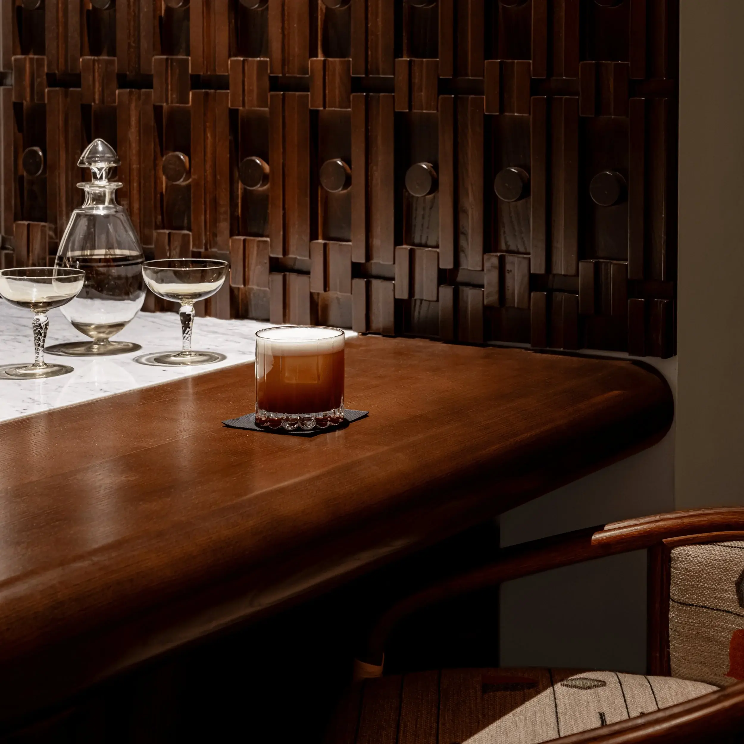 Bicchiere da cocktail marrone a strati con schiuma sul bancone del bar in legno vicino a due bicchieri da coupé vuoti.