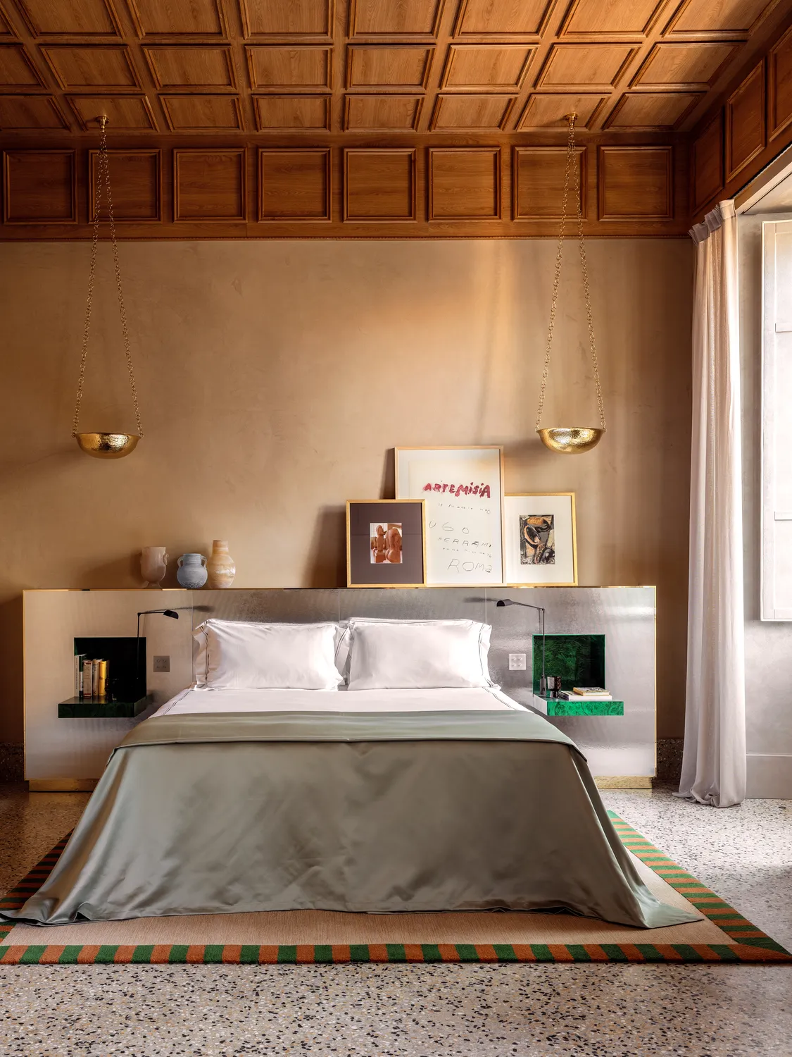 Camera da letto moderna con un grande letto, copriletto verde seta, soffitto in legno e opere d'arte incorniciate sopra la testiera.