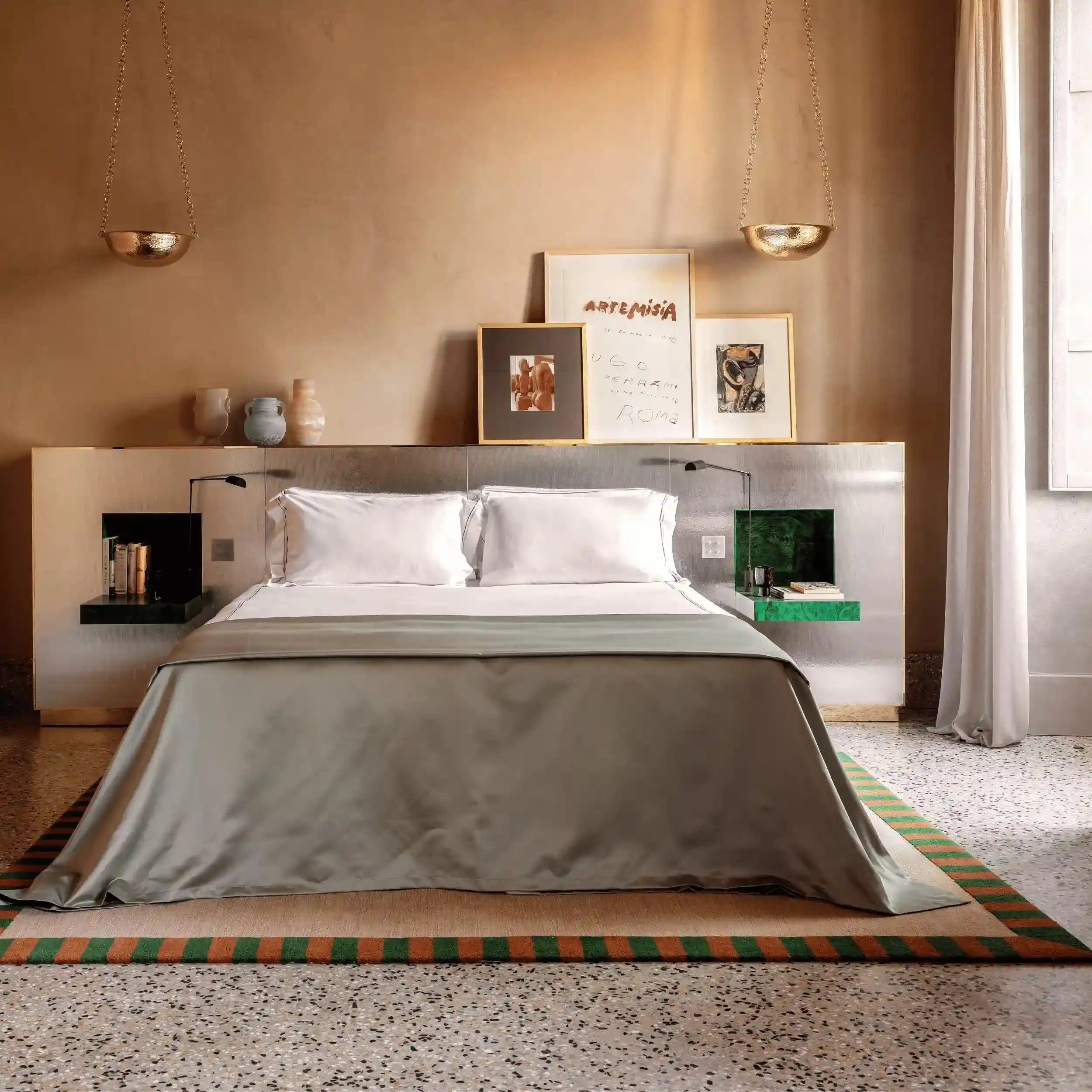 Modern bedroom with a large bed, neutral tones, framed art above, and hanging gold pendant lights.