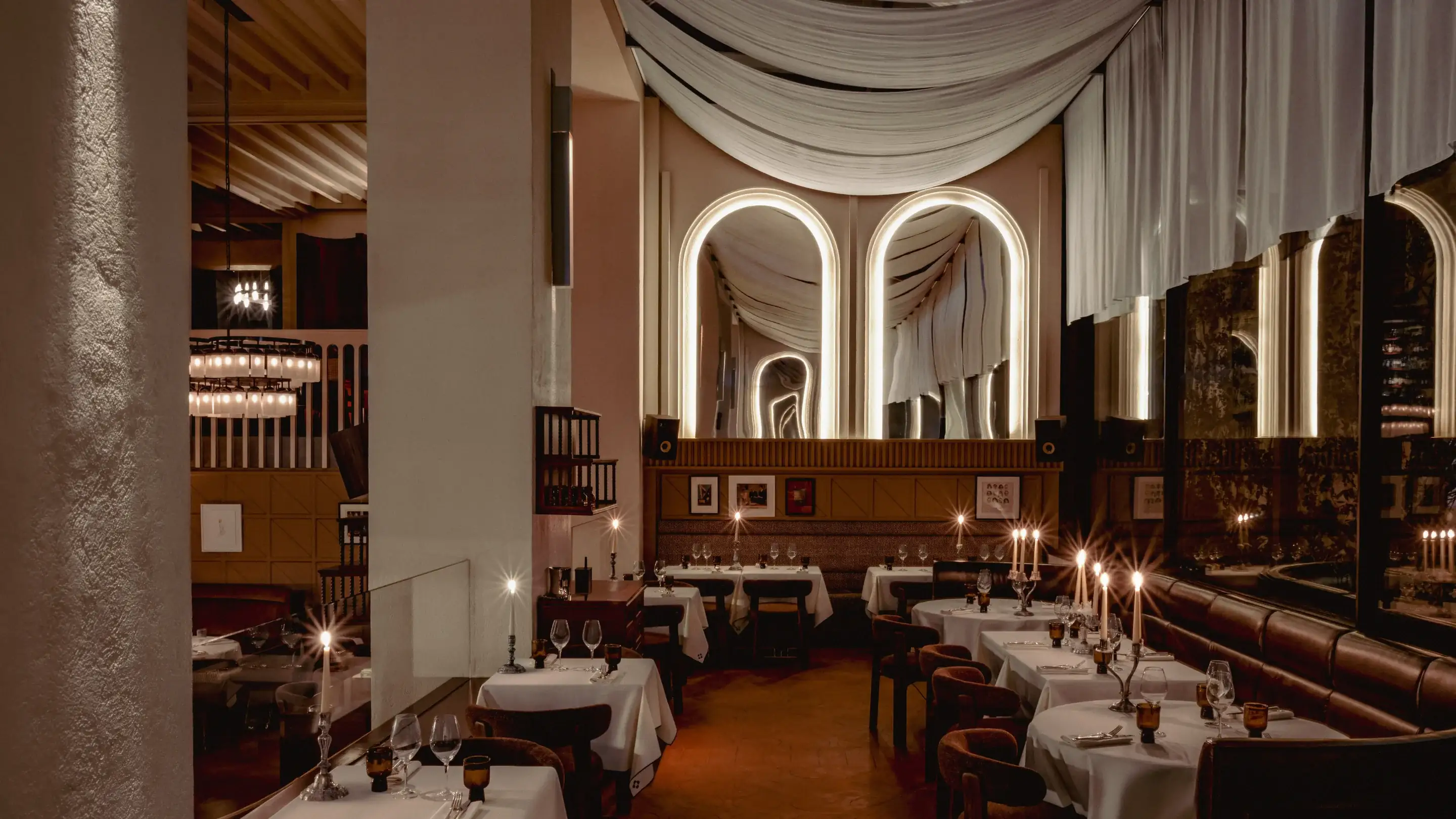 Accogliente ristorante poco illuminato con tovaglie bianche, candele ed eleganti specchi alle pareti.