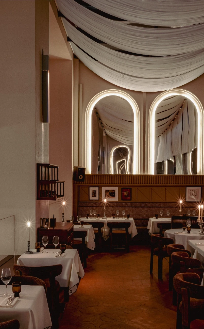 Elegante interno del ristorante con tovaglie bianche, lume di candela, specchi ad arco e soffitto drappeggiato in tessuto.