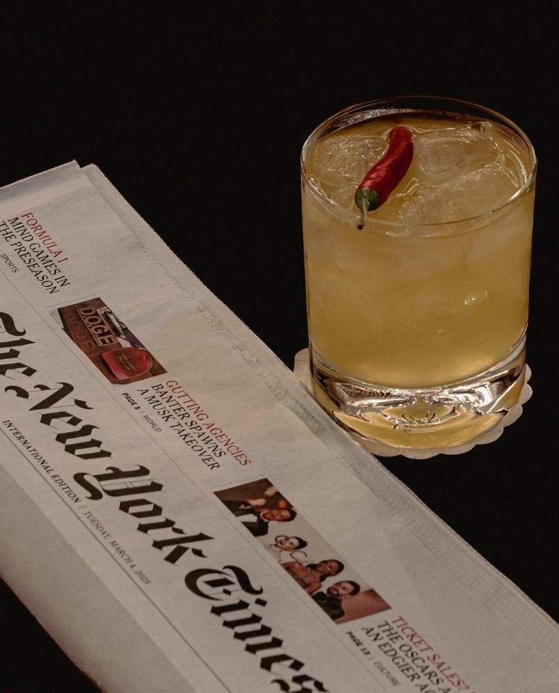 Bicchiere di cocktail ghiacciato guarnito con peperoncino rosso accanto a un giornale piegato del New York Times.
