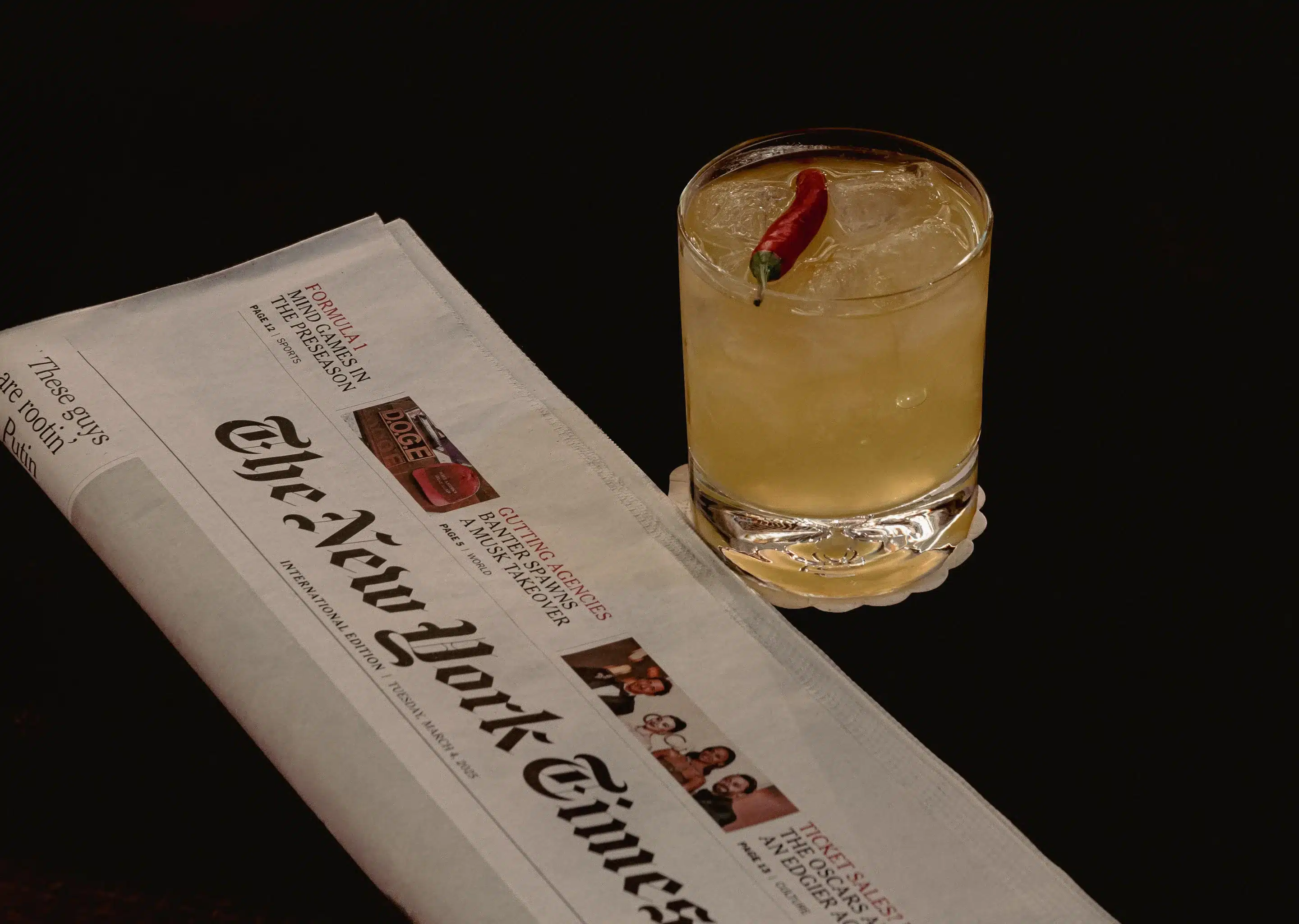 Giornale e un bicchiere di bevanda ghiacciata guarniti con peperoncino rosso su sfondo scuro.