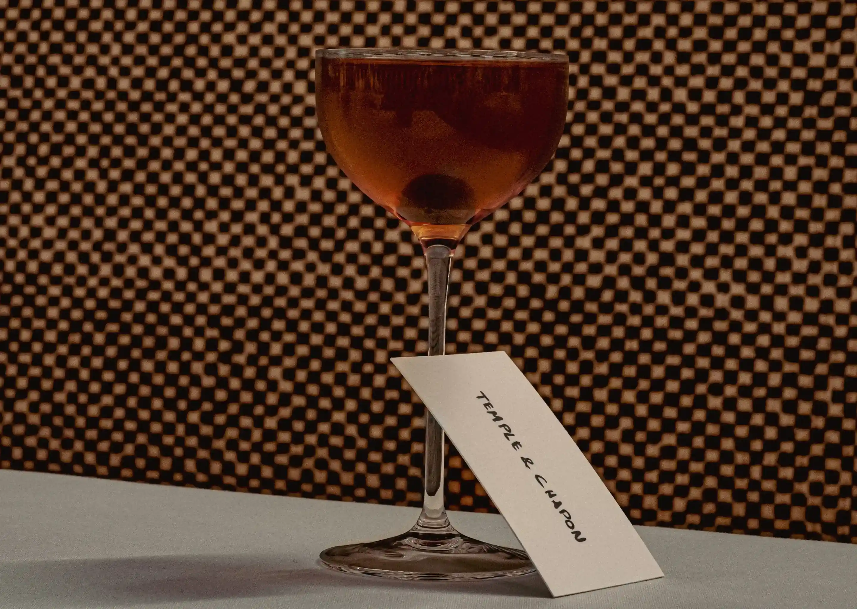 Cocktail glass with amber drink and cherry, tagged with card labeled Temple & Chapon.