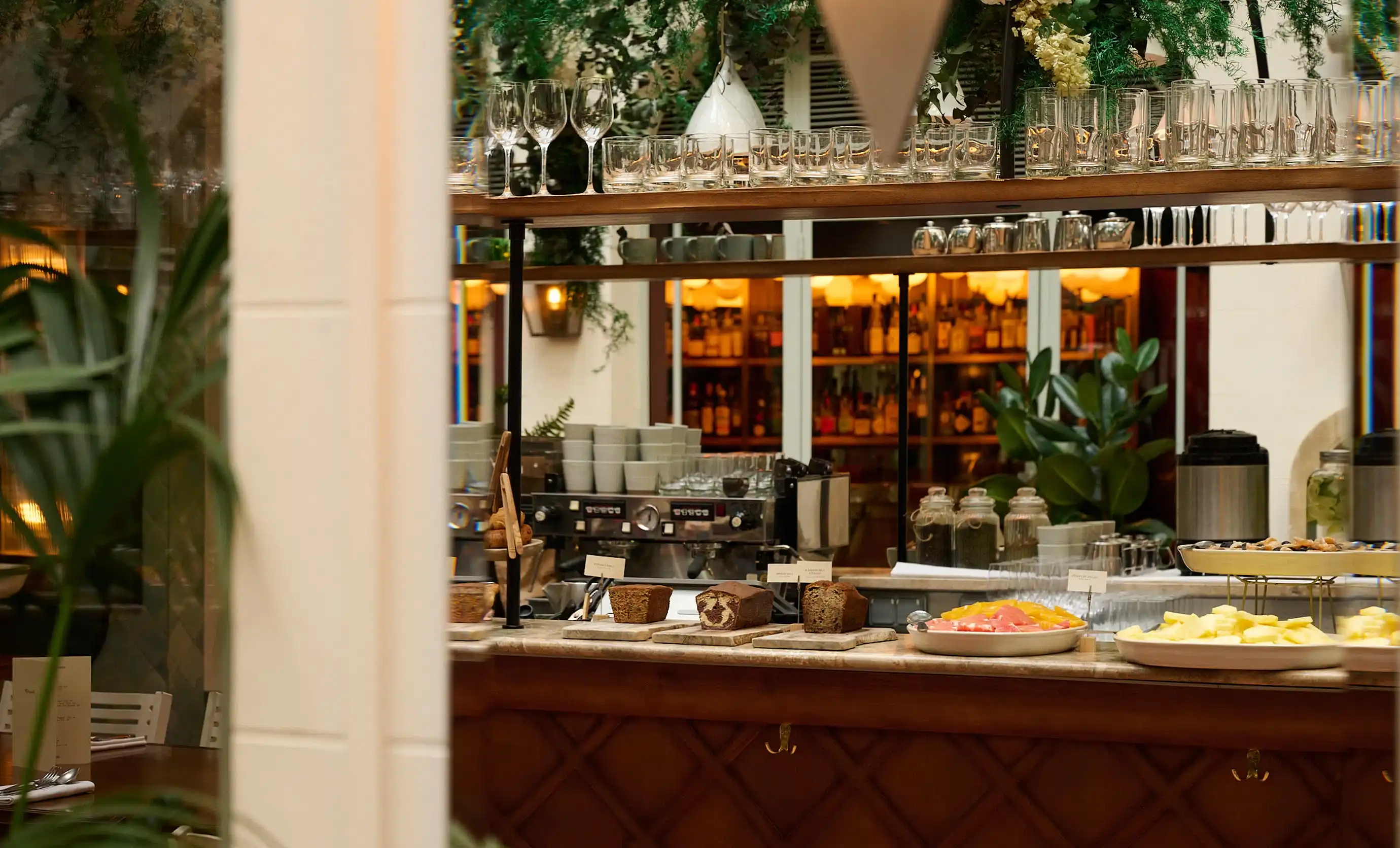 Counter with breads, plates of fruit, glassware, and coffee machine in a warmly lit café or restaurant.