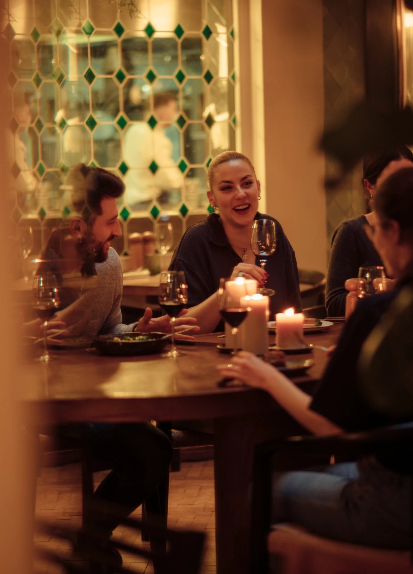 Group of friends enjoying dinner and wine by candlelight at a cozy restaurant table.