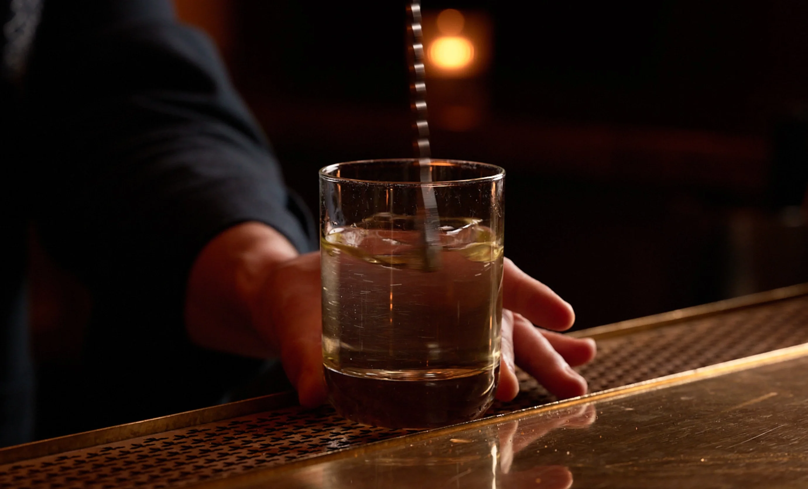 Mexendo manualmente uma bebida transparente com gelo em um copo no balcão de um bar.