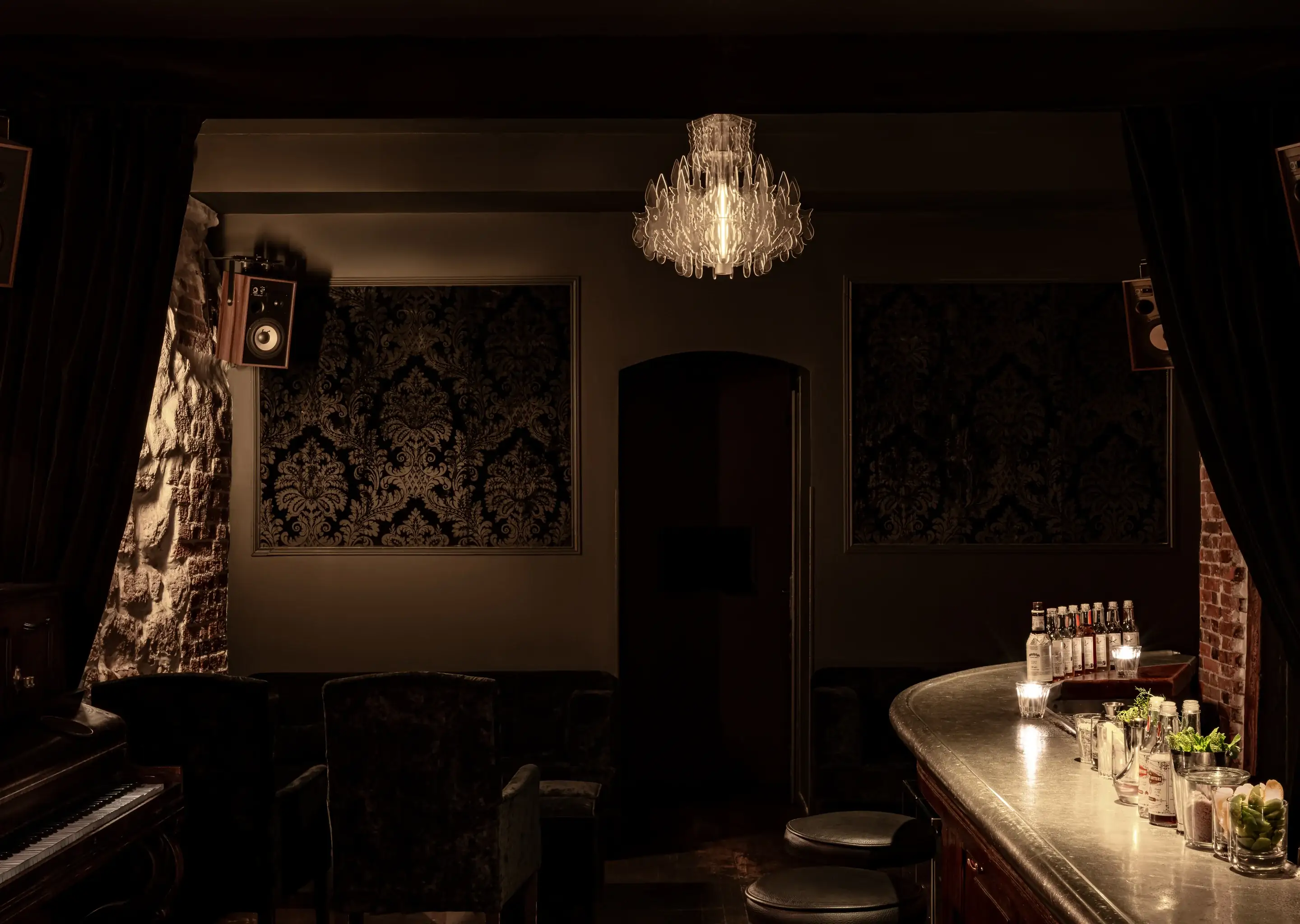 Bar vintage mal iluminado com balcão curvo, bancos, painéis de parede estampados e um lustre.