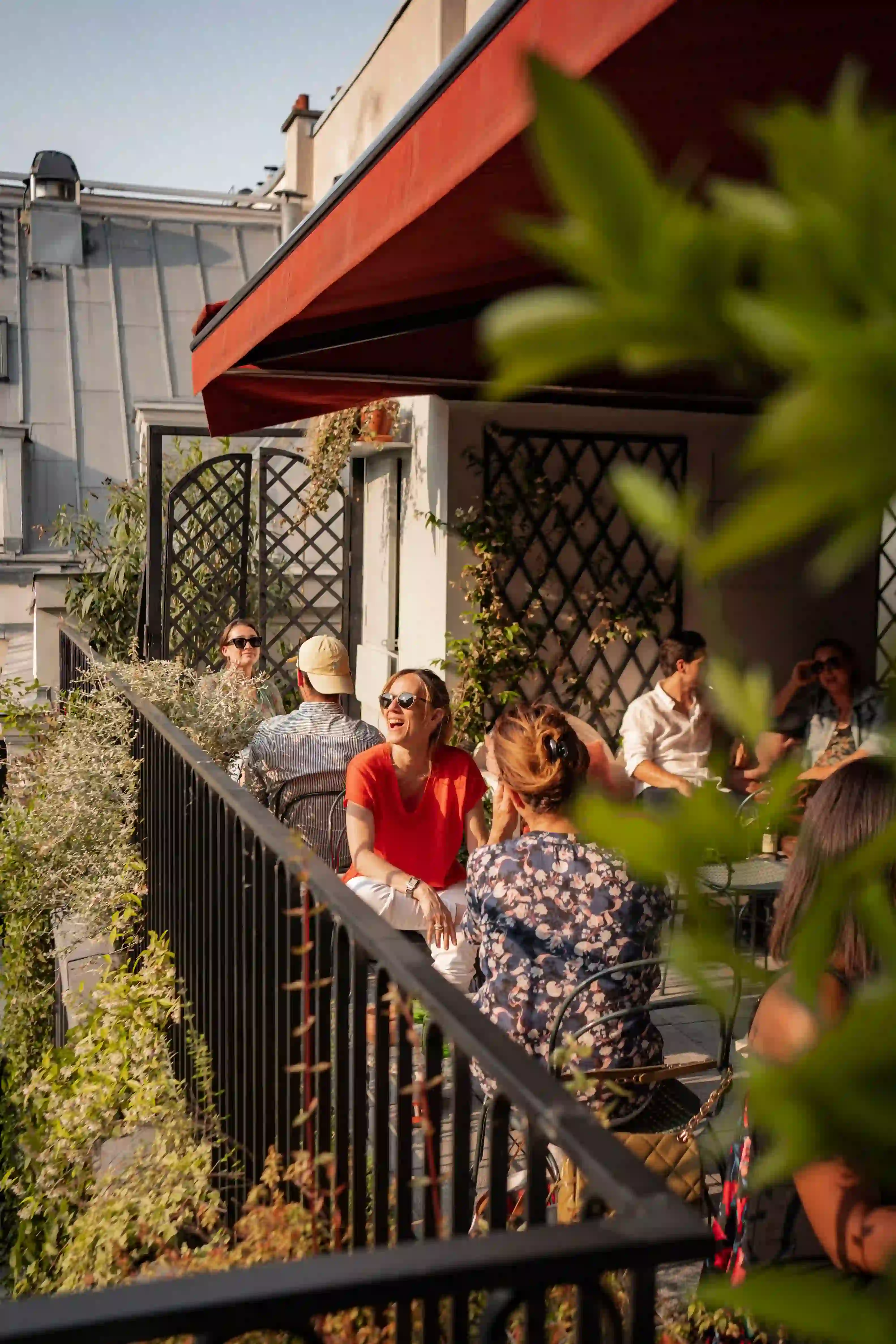 Persone che chiacchierano e si rilassano su una soleggiata terrazza all'aperto con piante e mobili da giardino.