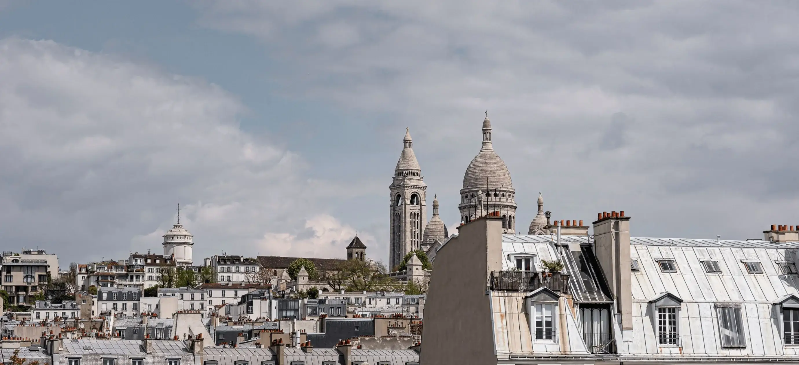 Paisagem urbana com telhados e a distinta cúpula e torre de uma basílica histórica sob um céu nublado.