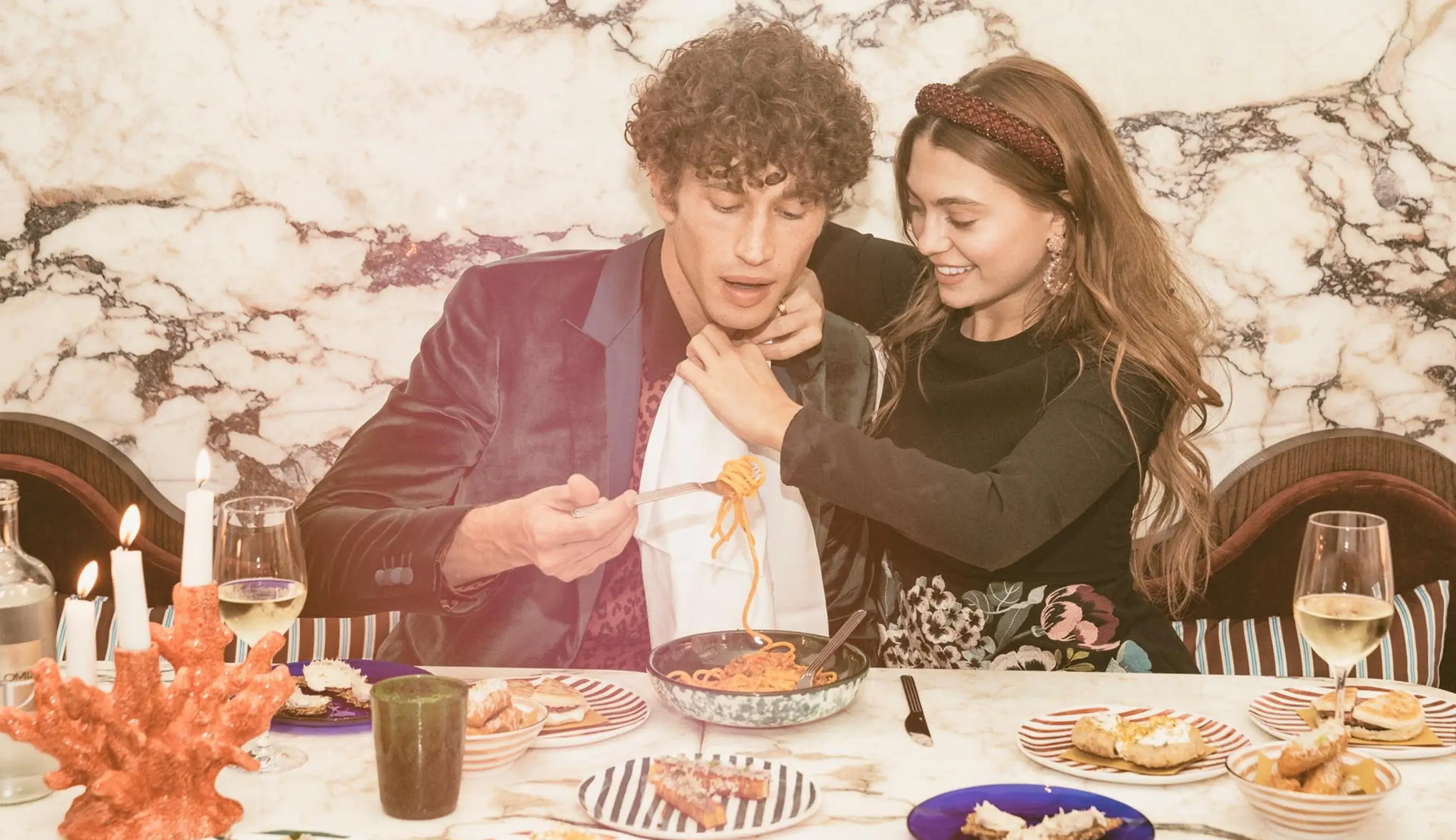 Casal desfrutando de uma refeição; mulher ajuda homem com guardanapo enquanto ele come macarrão com espaguete.