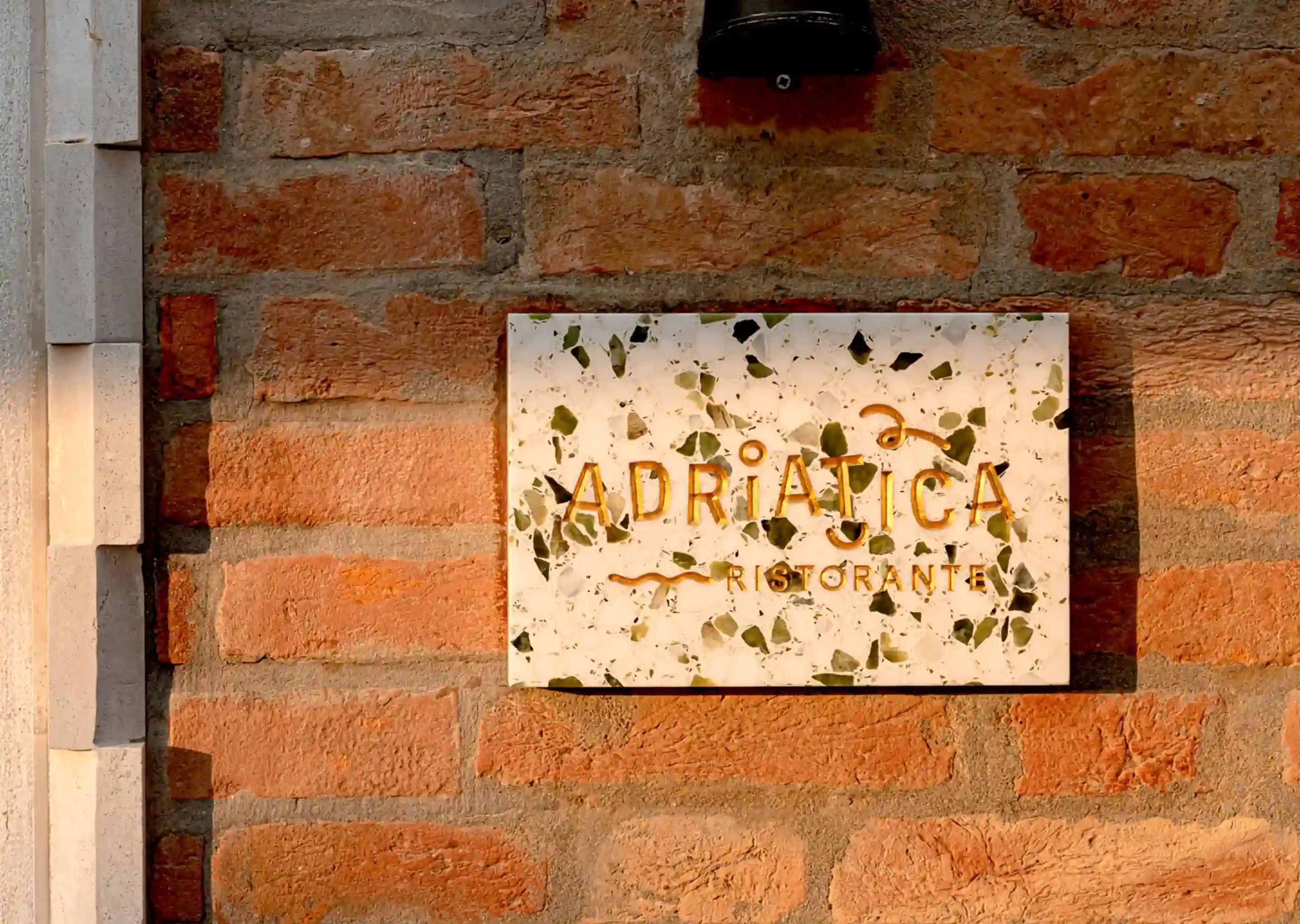 Placa de mármore com manchas verdes e pretas onde se lê “ADRIATICA RISTORANTE” em uma parede de tijolos.