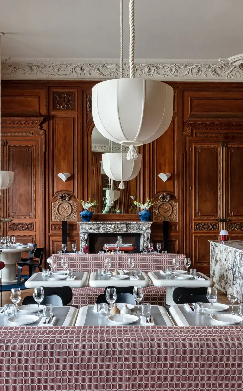 Elegante interno del ristorante con pareti rivestite in legno, camino decorato, panche a motivi geometrici e lampade bianche a sospensione.