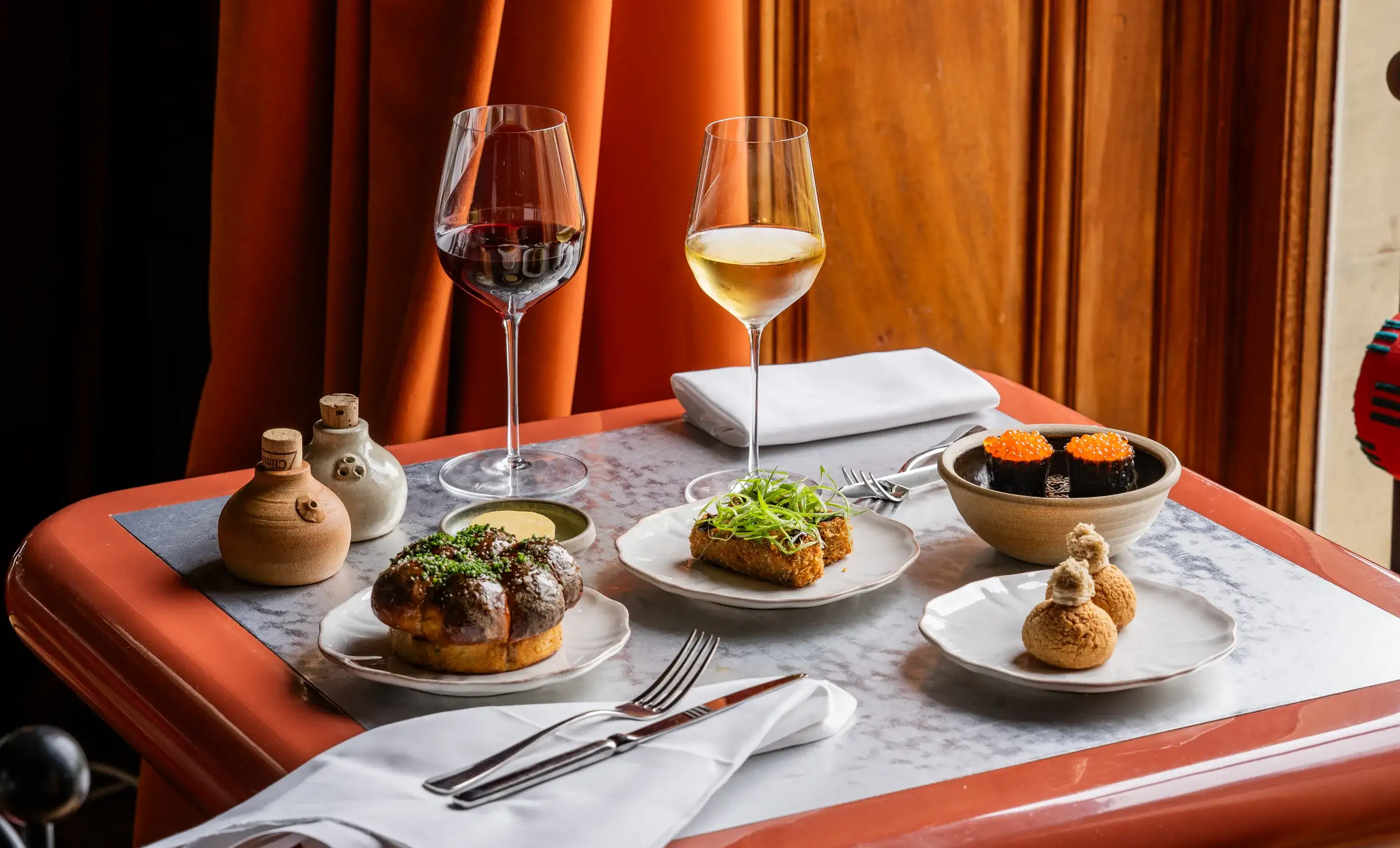 Tavolo con piatti gourmet tra cui due bicchieri di vino rosso e bianco in un accogliente ambiente da ristorante.