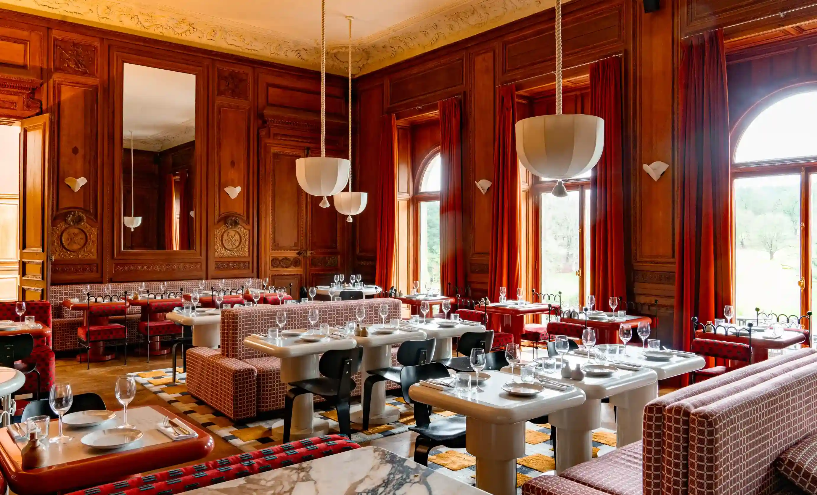 Elegante interno del ristorante con pannelli in legno, tende rosse, tavoli apparecchiati e sedie moderne.