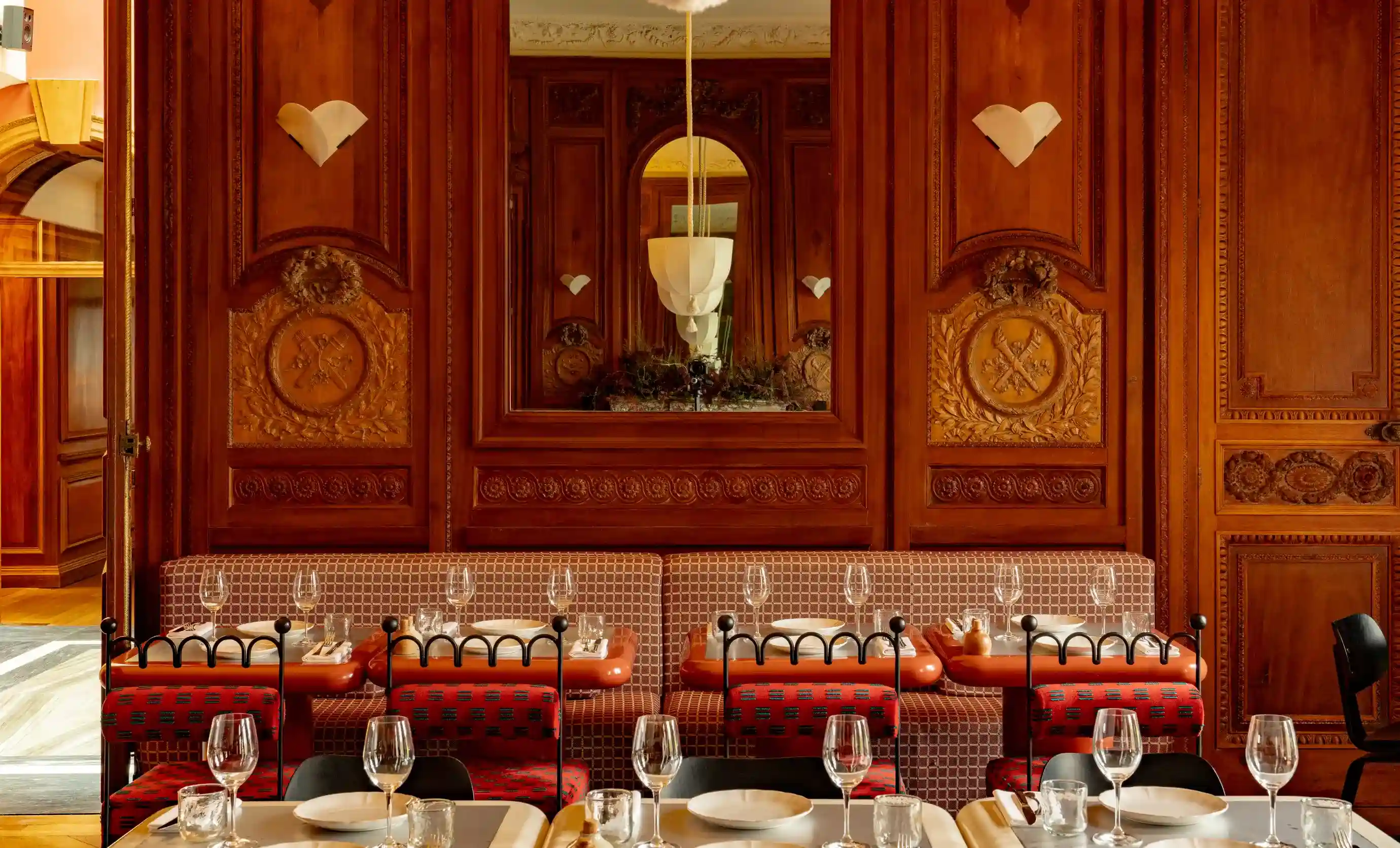 Elegante interno del ristorante con sedie rosse e nere, tavoli apparecchiati e pareti decorate con pannelli in legno con specchio.