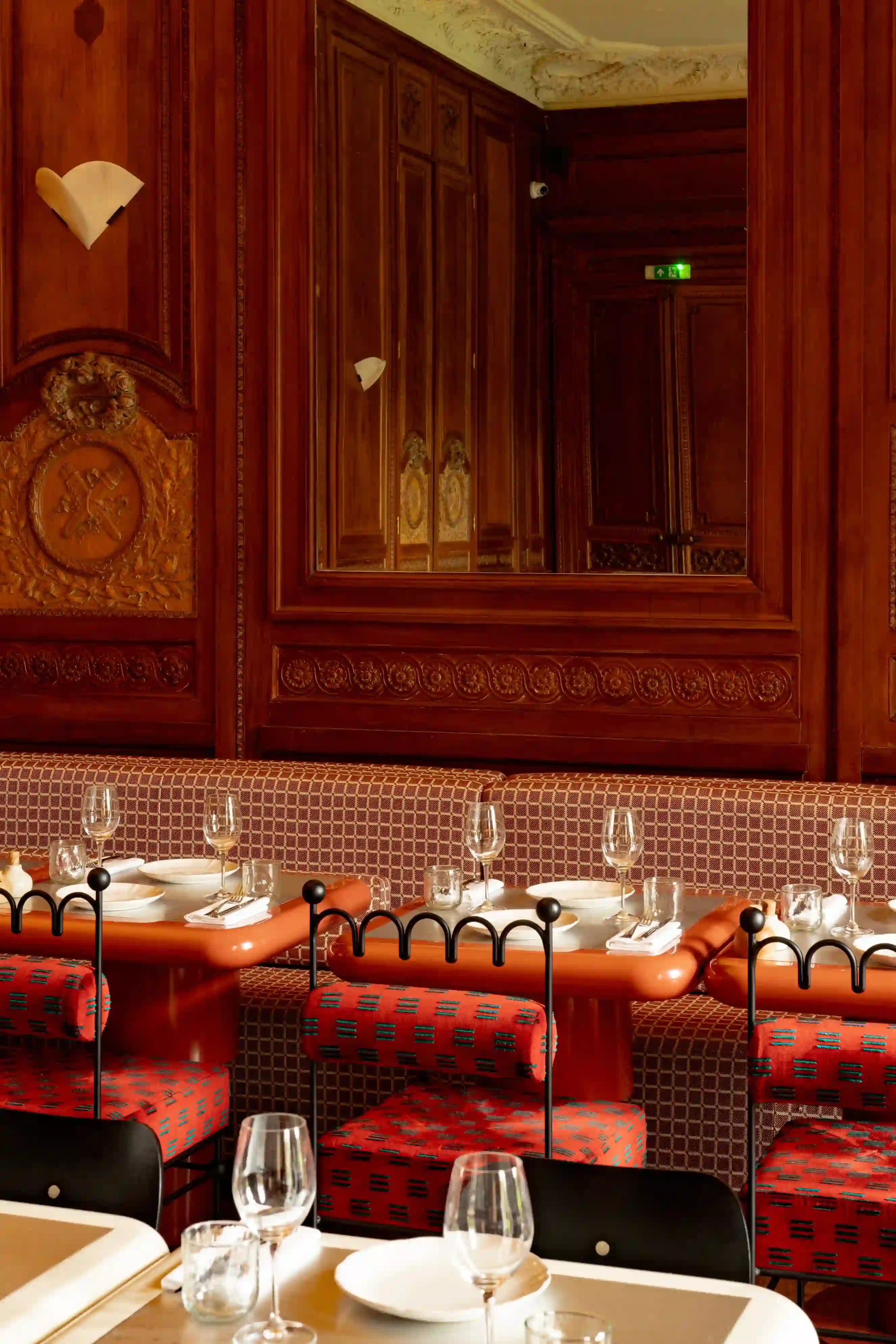 Eleganti posti a sedere da ristorante con sedie imbottite rosse, tavoli apparecchiati, pareti in pannelli di legno e un grande specchio.