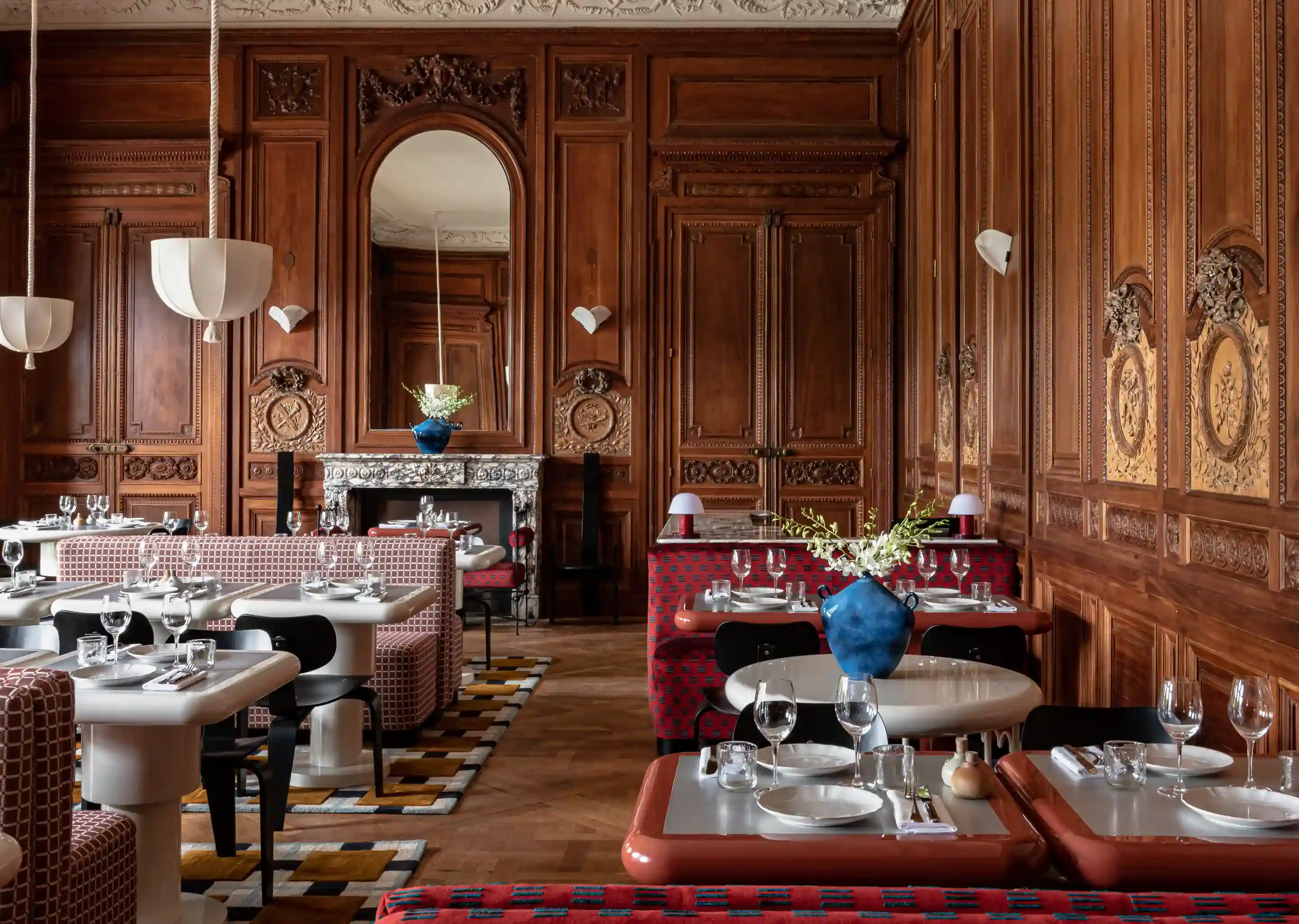 Elegante sala da pranzo con pareti in legno decorate, cabine a motivi geometrici, tavoli bianchi e vasi blu con fiori.