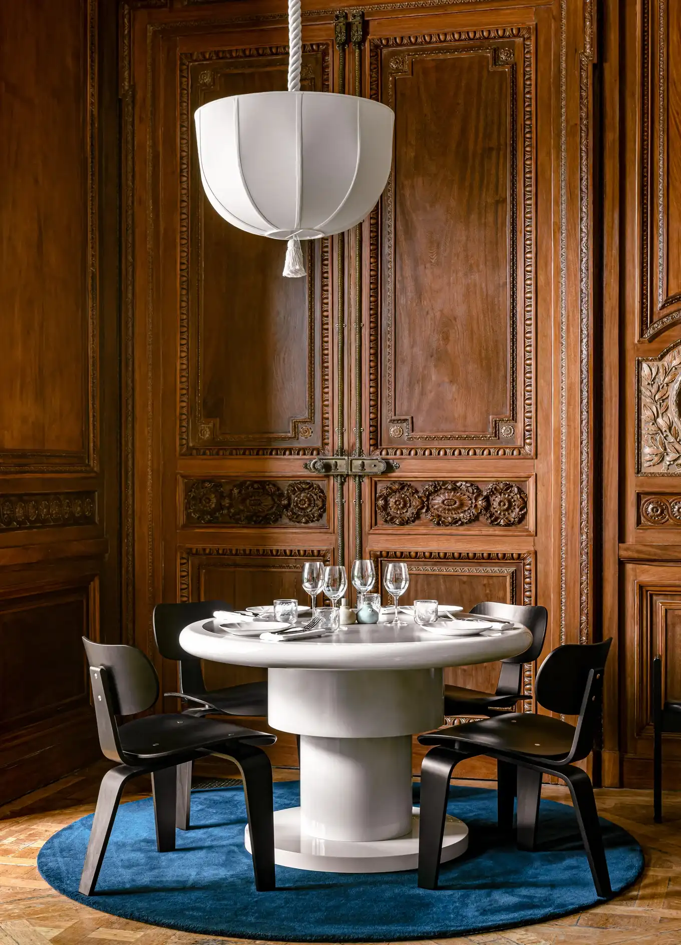 Tavolo da pranzo rotondo bianco con sedie nere su tappeto blu davanti a pareti decorate con pannelli in legno.