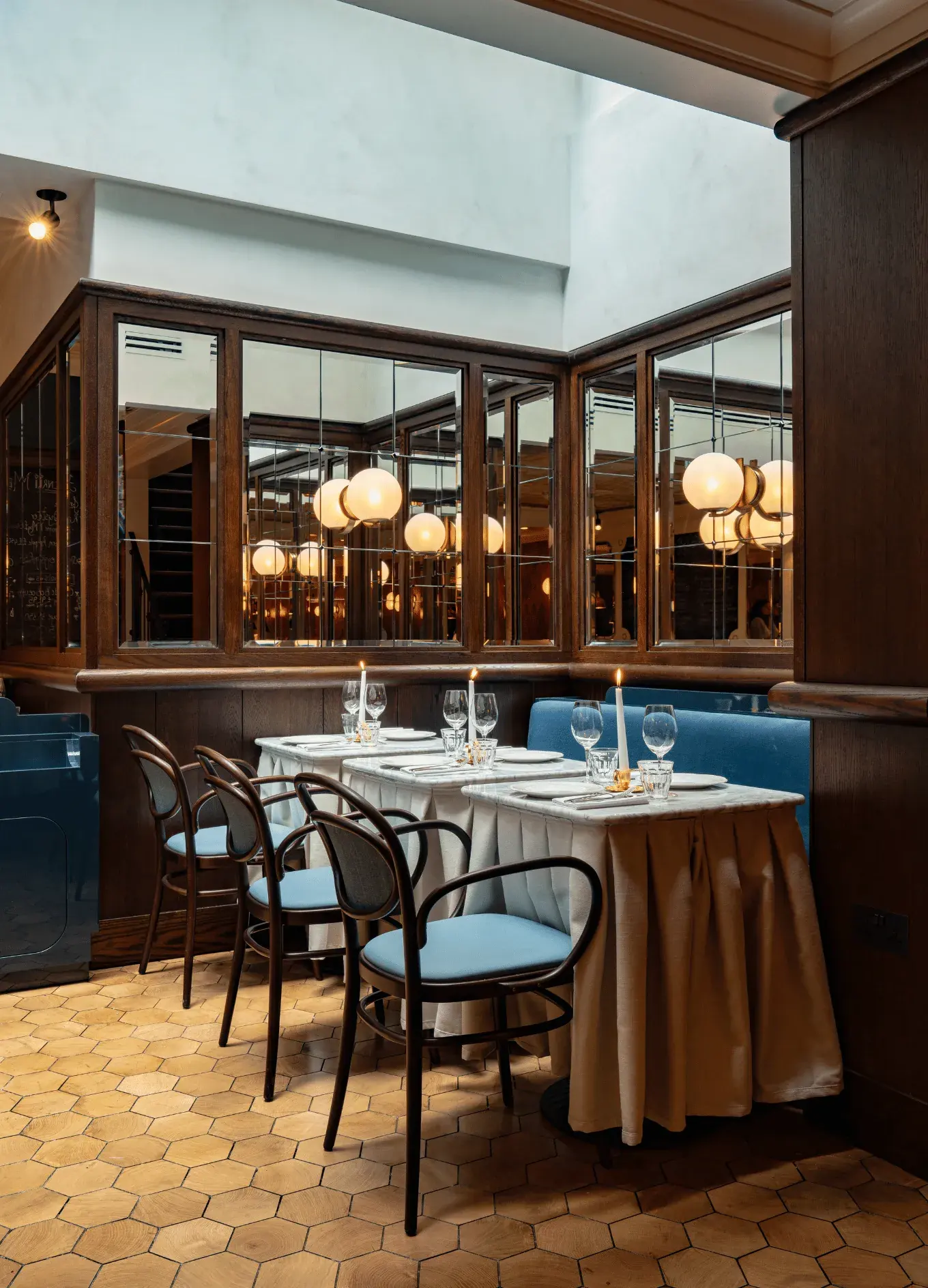 Elegante angolo ristorante con quattro tavoli apparecchiati con candele, bicchieri, sedili blu e pareti rivestite in legno.