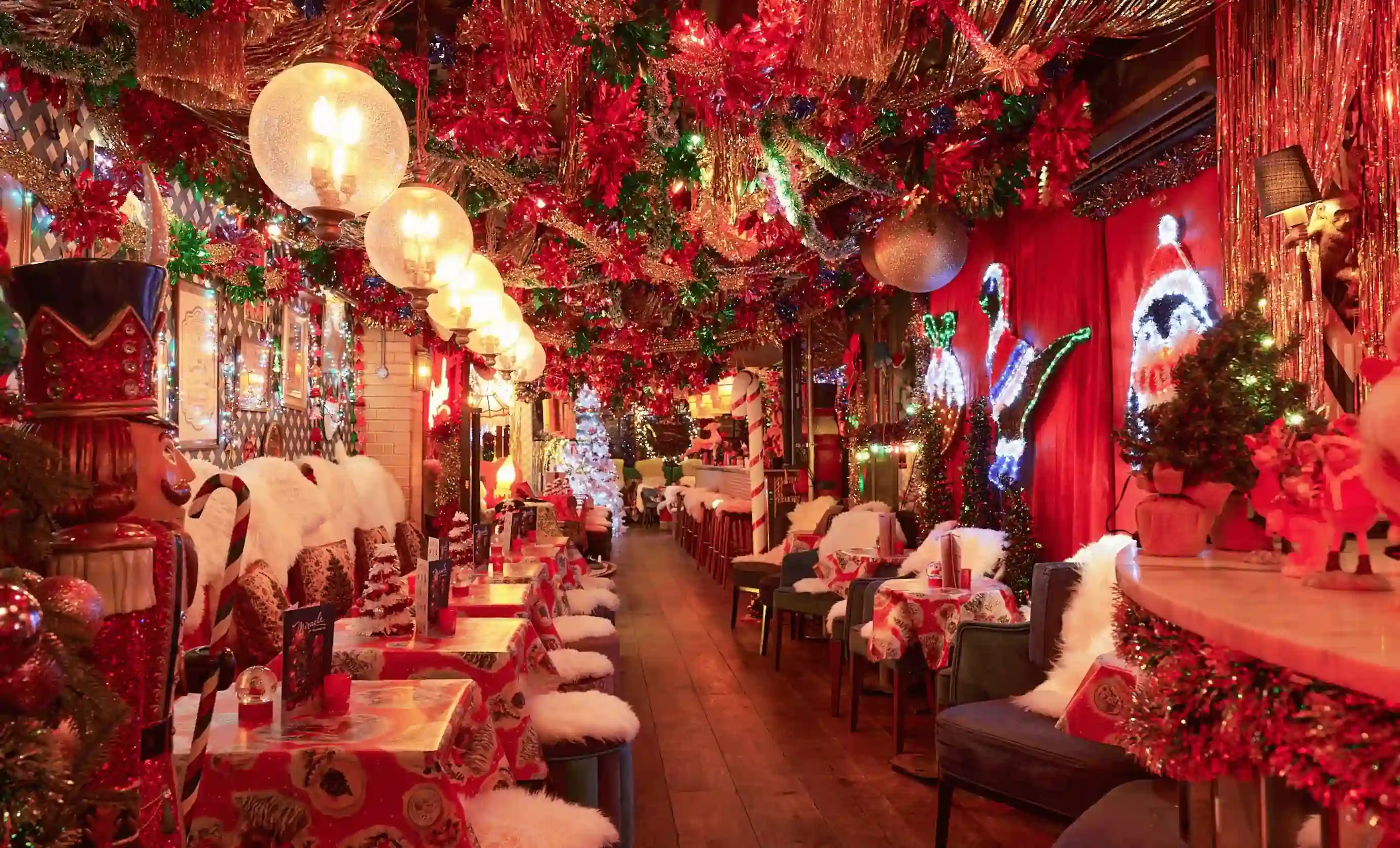 Espaço interno ricamente decorado com luzes de Natal, enfeites, quebra-nozes, guirlandas e toalhas de mesa festivas.