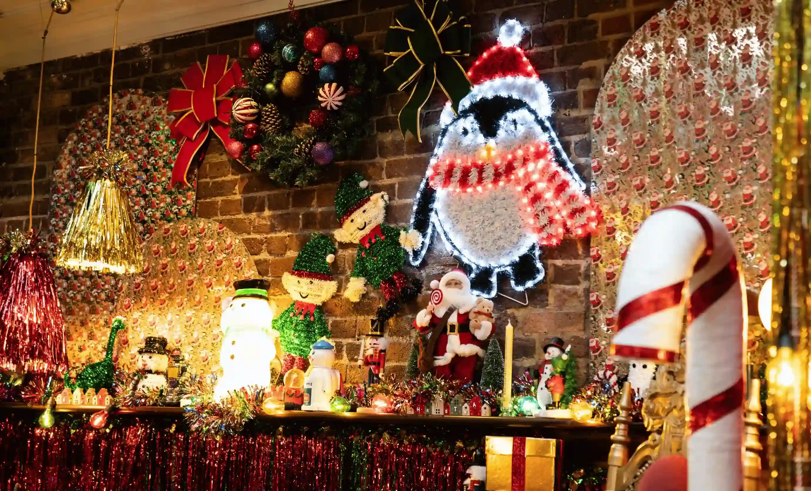 Prateleira festiva com decoração iluminada de pinguins, Papai Noel, duendes, bonecos de neve, coroas de flores e bastões de doces.