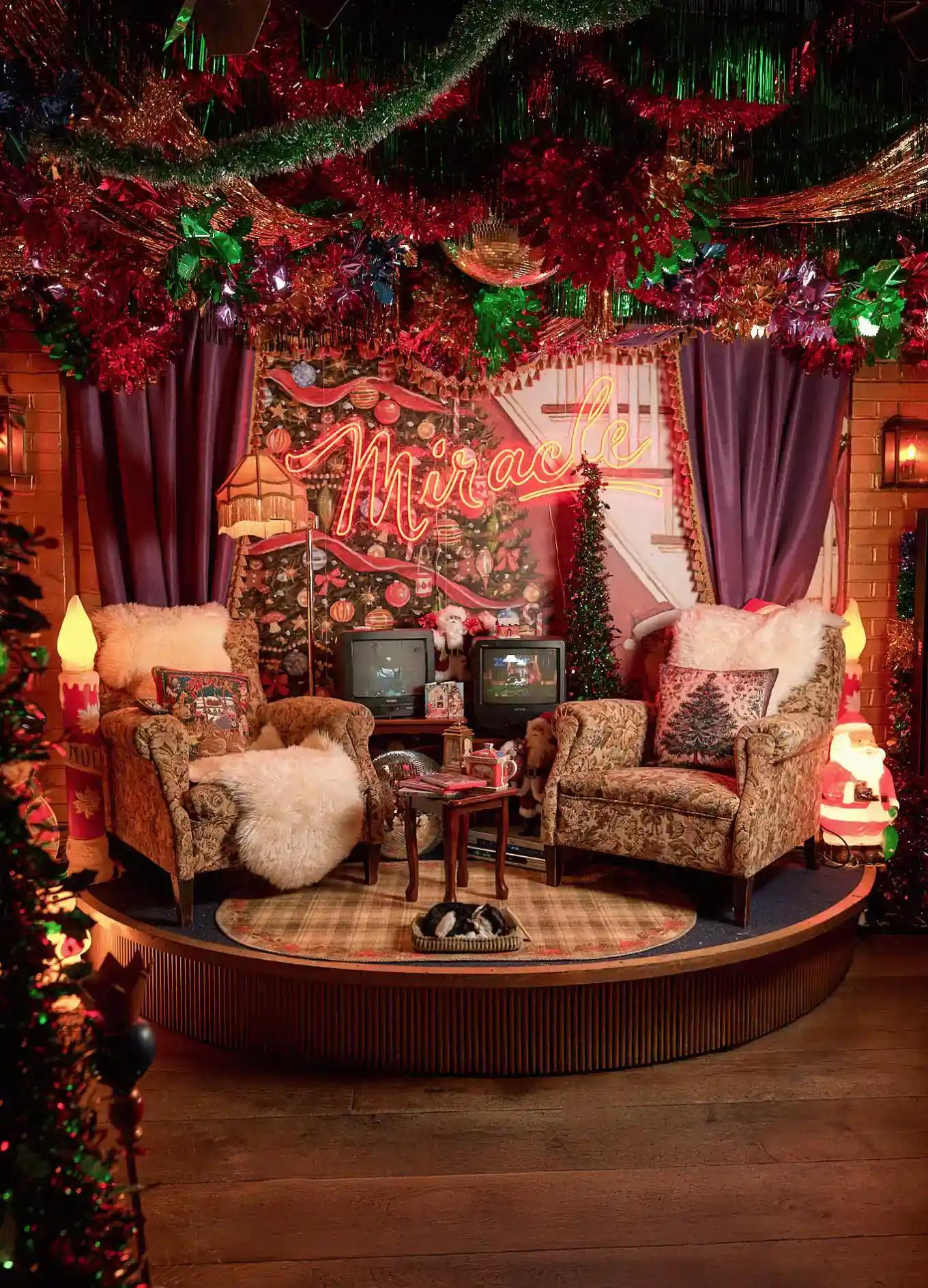 Configuração aconchegante de sala de estar de férias com duas poltronas, decorações de Natal e uma placa de néon dizendo Miracle.