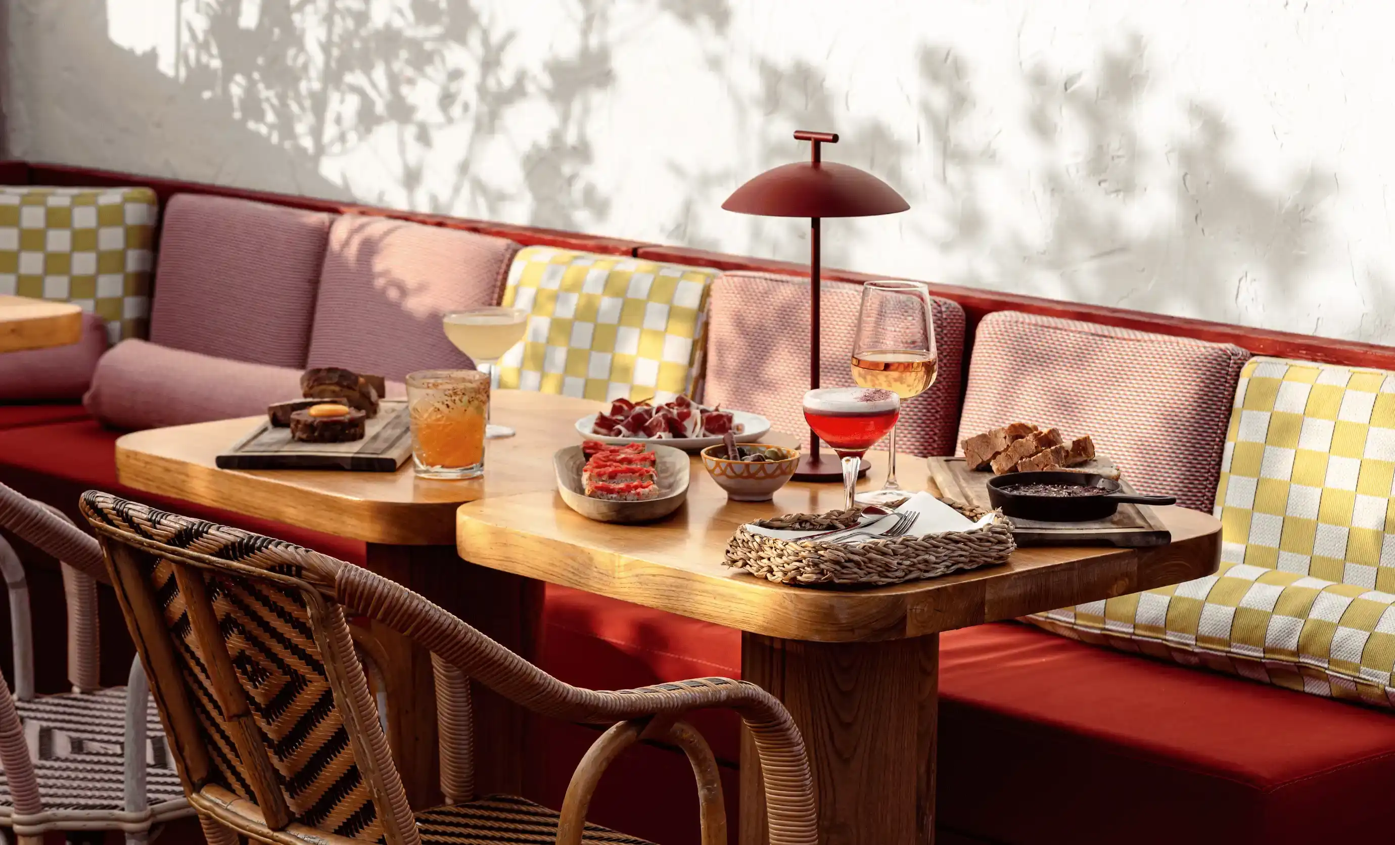 Tavolino da caffè in legno con cocktail, antipasti, cestino intrecciato e panca imbottita con cuscini a motivi geometrici.