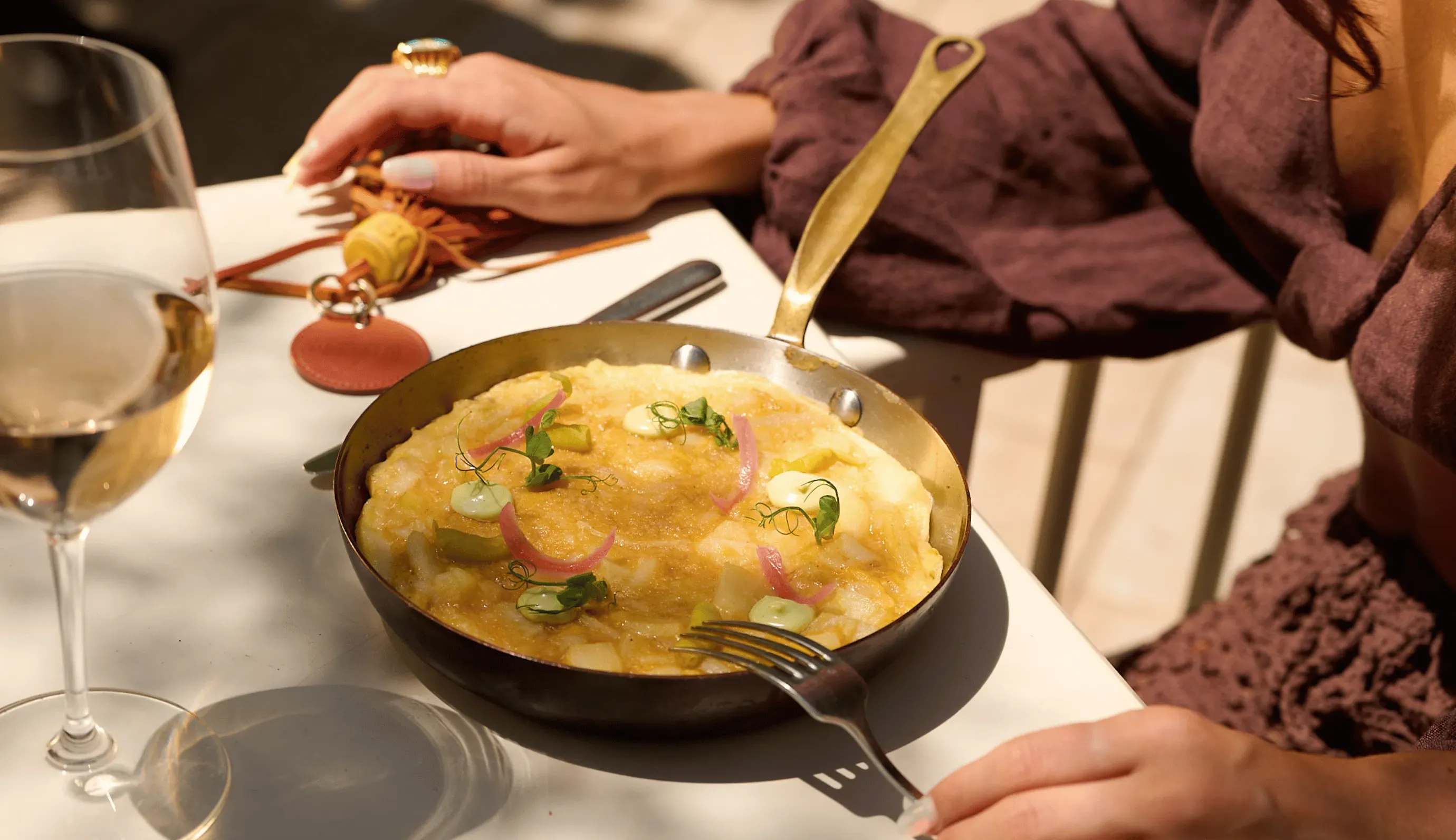 Delicata frittata guarnita con erbe aromatiche e cipolle marinate in padella accanto a un bicchiere di vino bianco.