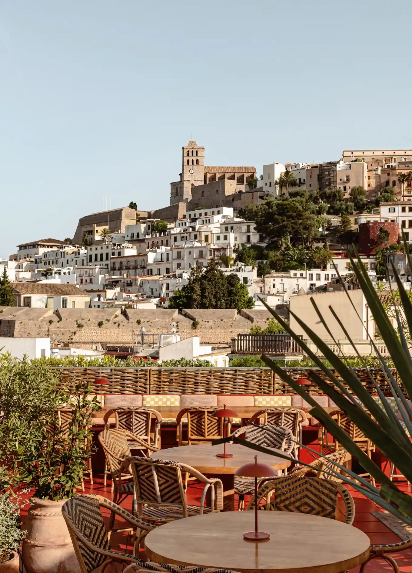 Outdoor terrace with tables and chairs overlooking white buildings and a stone tower on a hill.