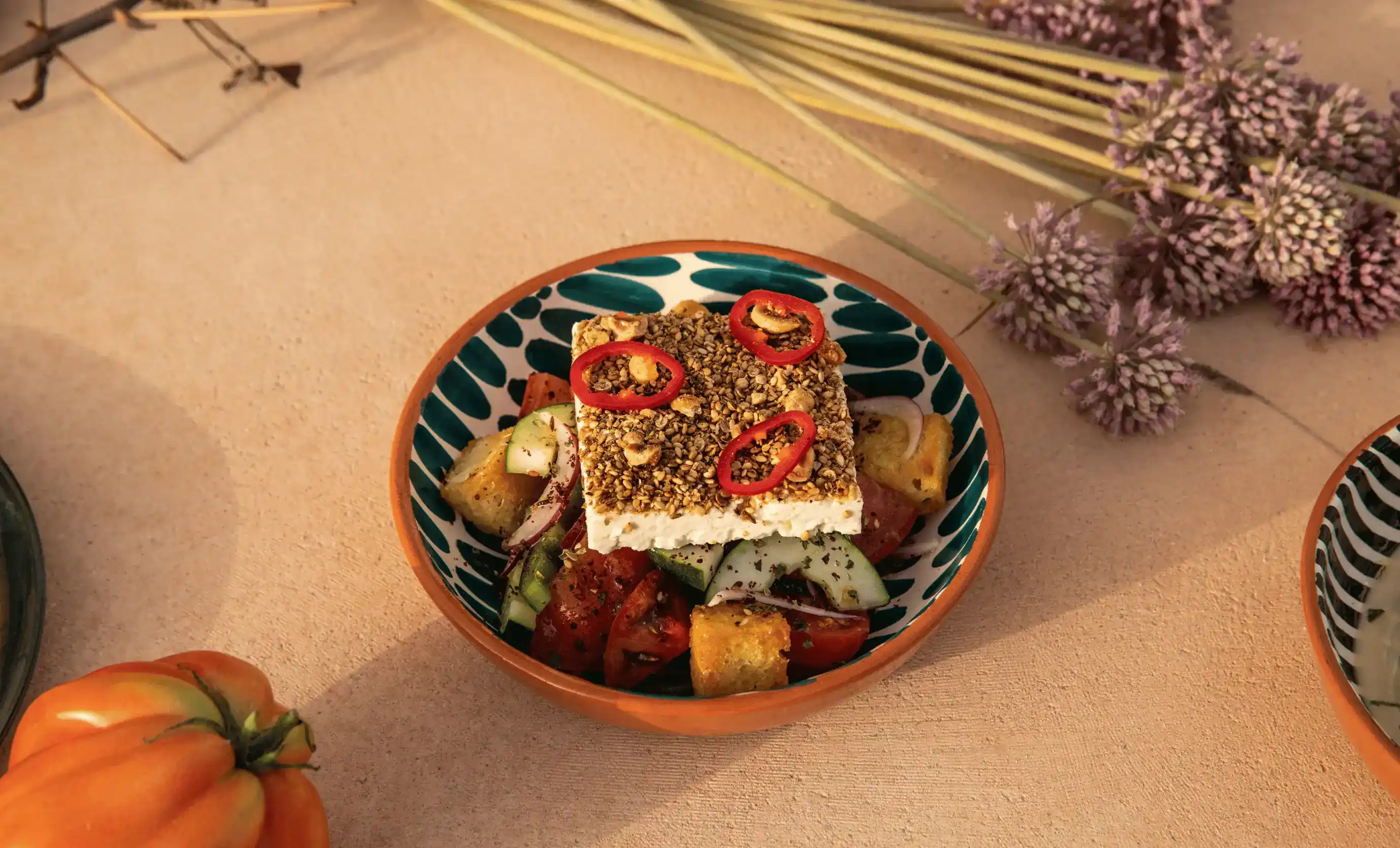 Insalata greca con formaggio feta condita con noci e fette di peperoncino rosso in una ciotola decorativa.
