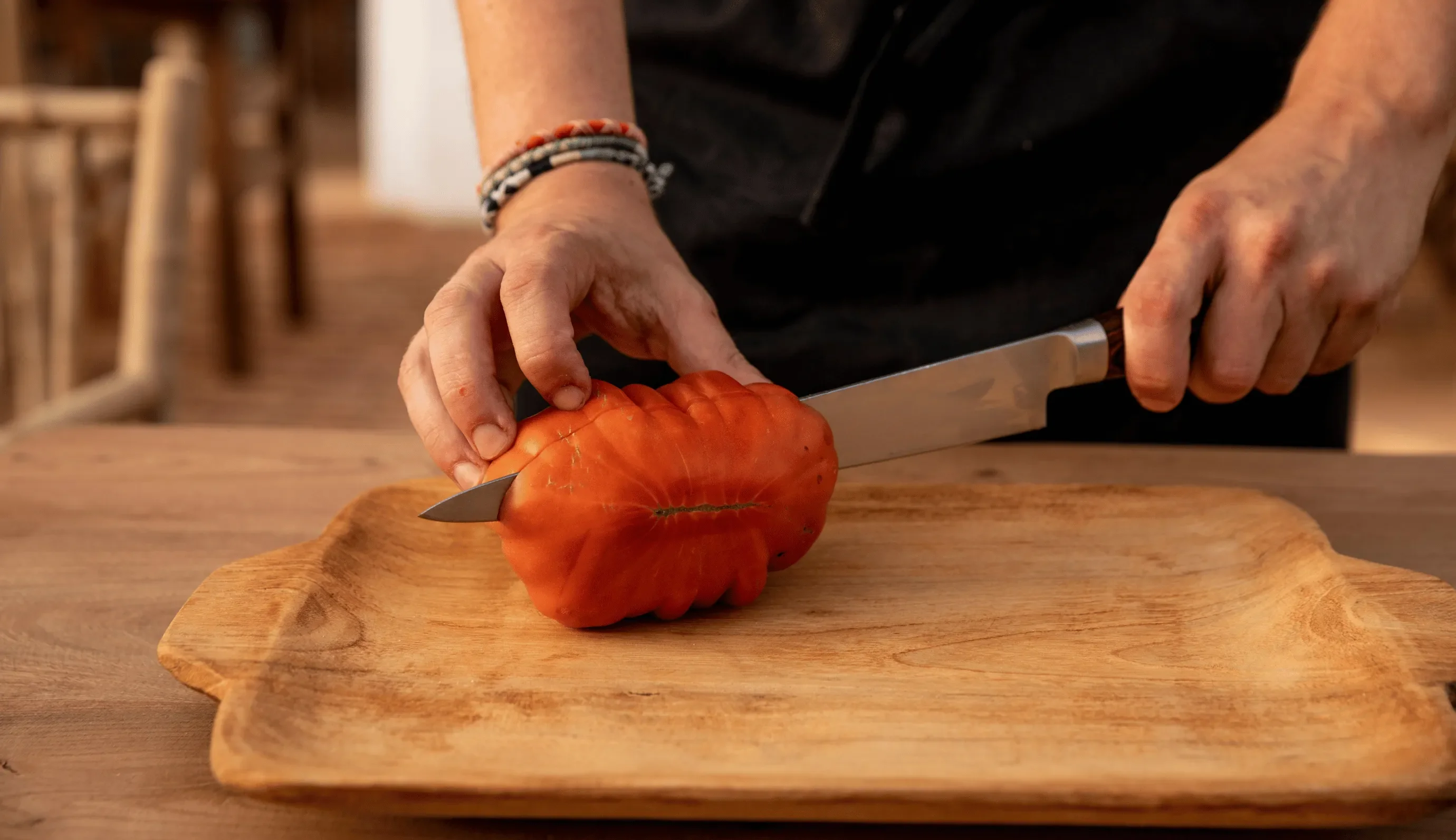 Persona che affetta un grosso pomodoro rosso a coste su un tagliere di legno.