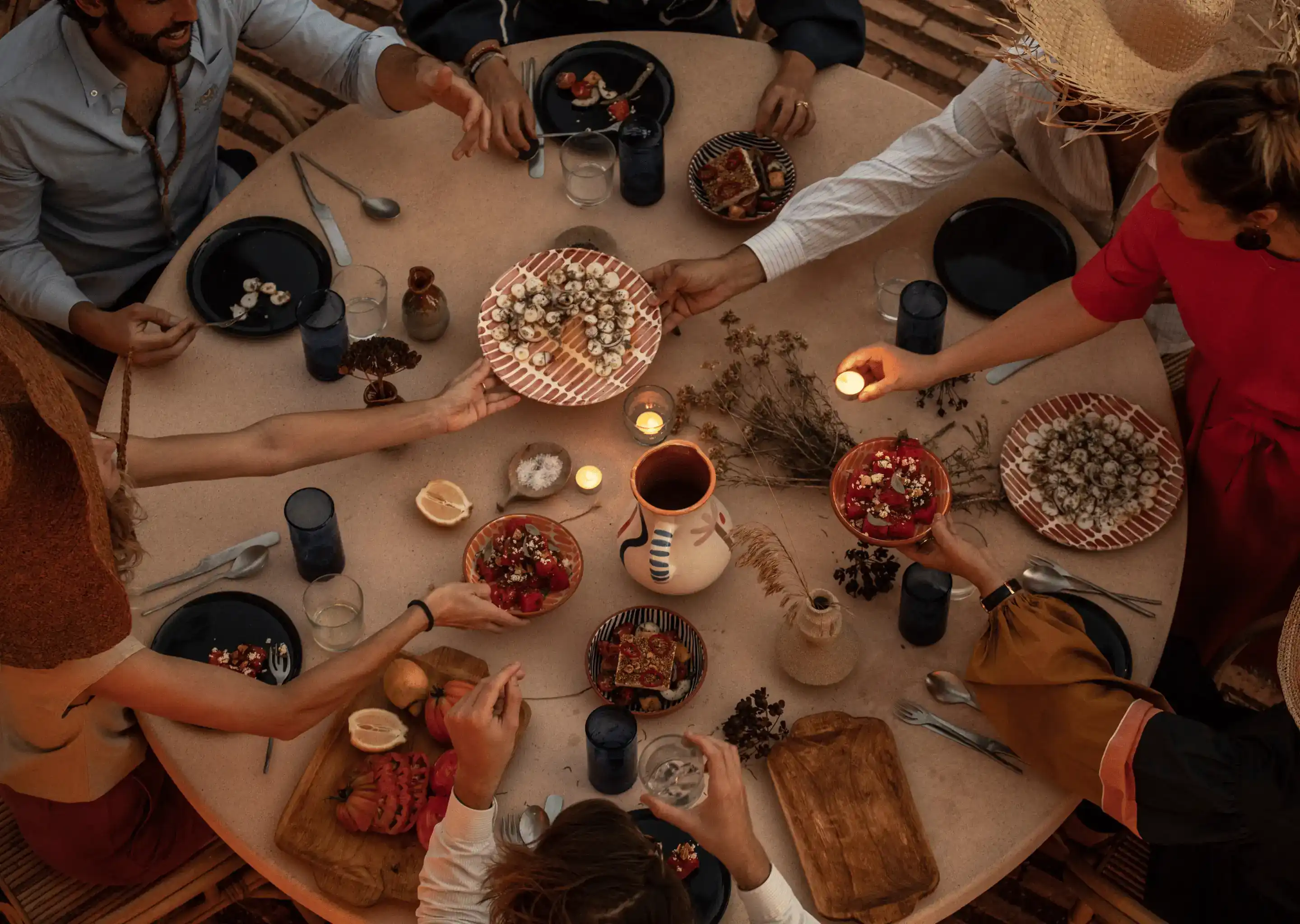 Vista dall'alto di persone che condividono cibo e bevande attorno a una tavola rotonda con piatti e candele.