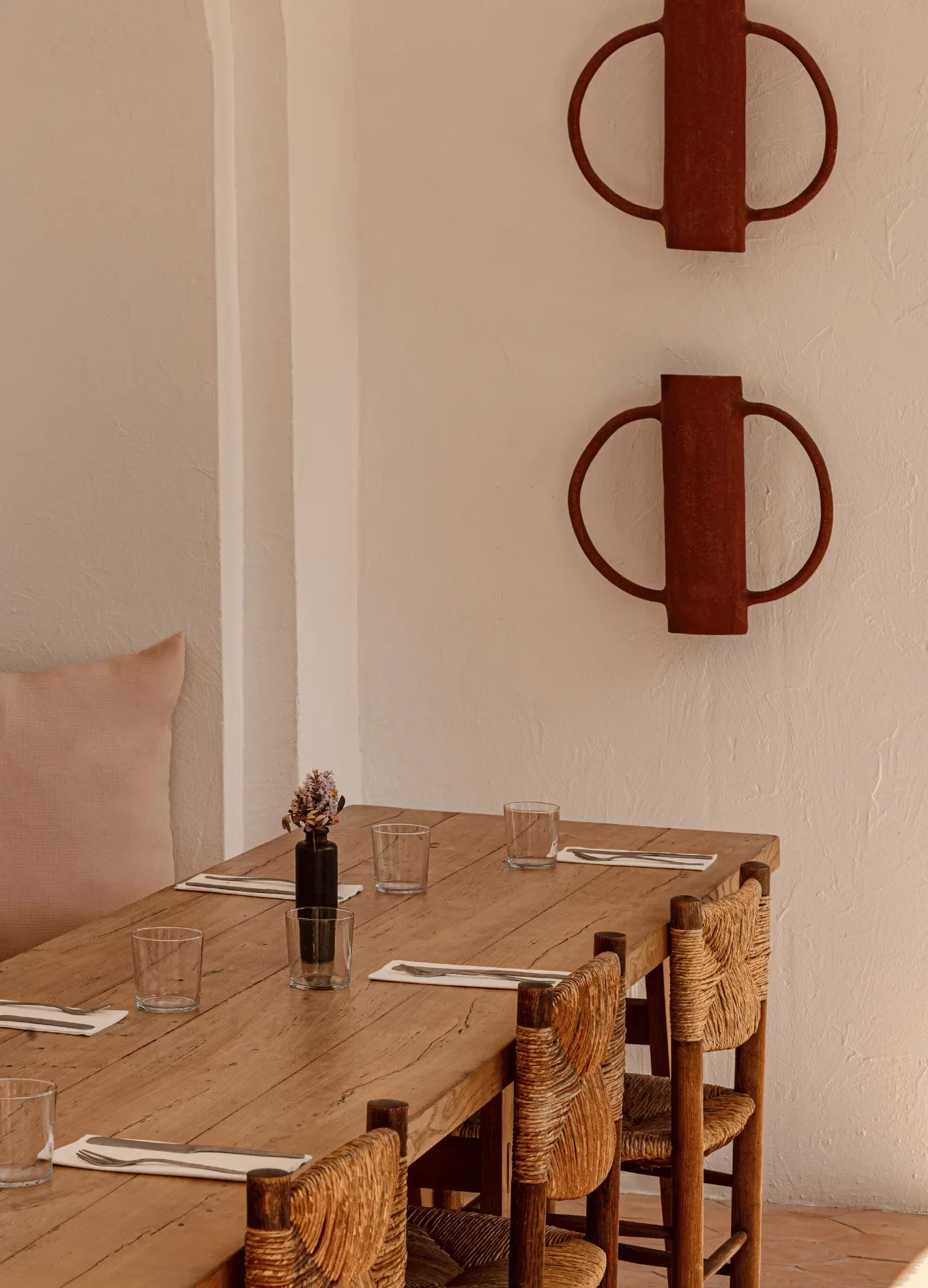 Tavolo da pranzo in legno per sei persone con sedie intrecciate e un piccolo vaso nero con fiori secchi.