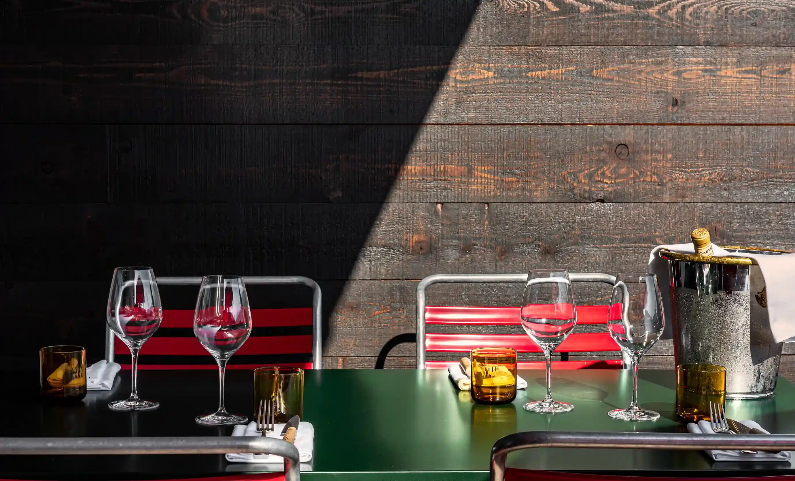 Tavoli da ristorante all'aperto con bicchieri da vino, bicchieri ambrati, posate e un secchio per champagne.