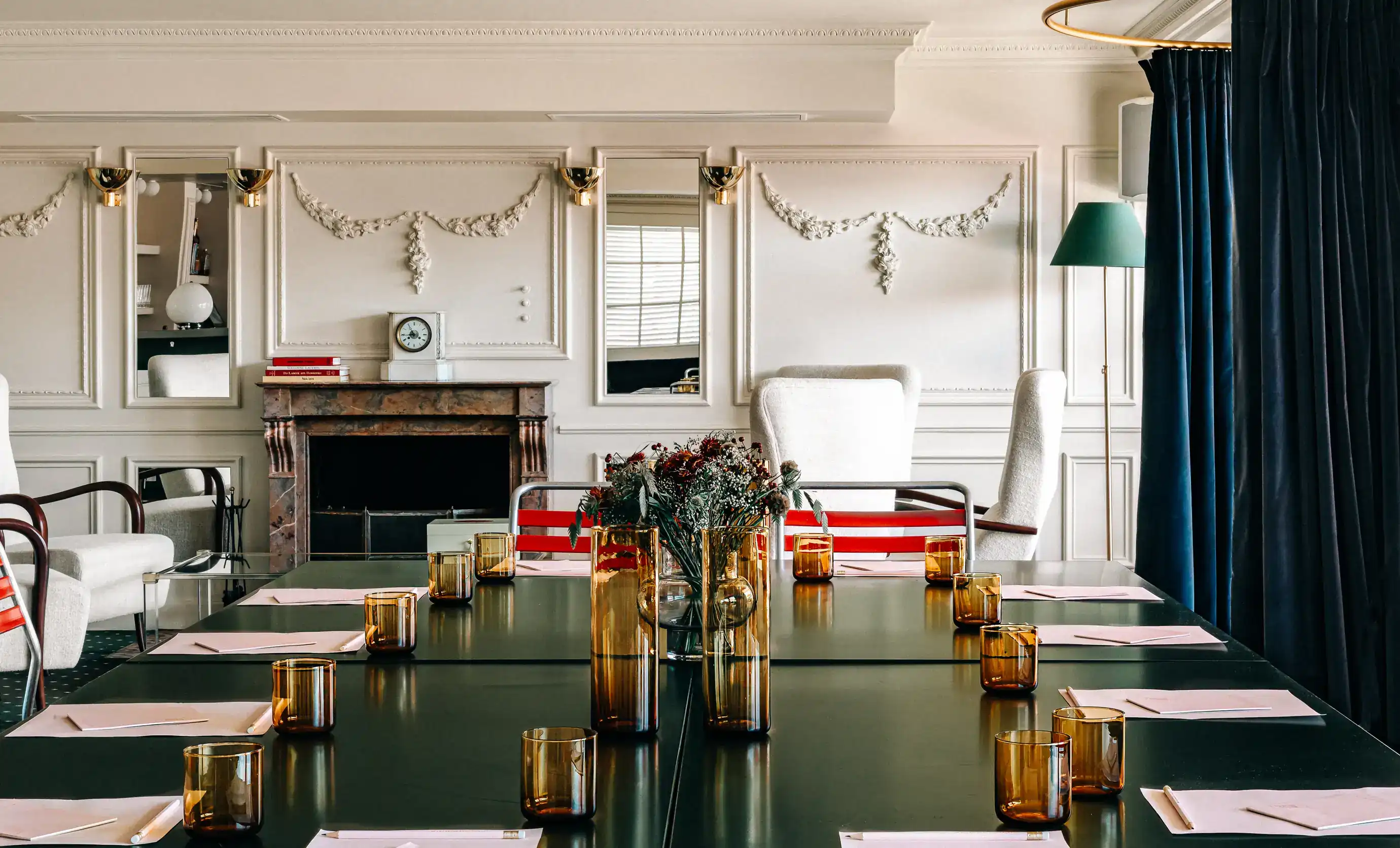 Elegante sala riunioni con tavoli scuri, bicchieri ambrati, sedie bianche, fiori e decorazioni murali classiche.