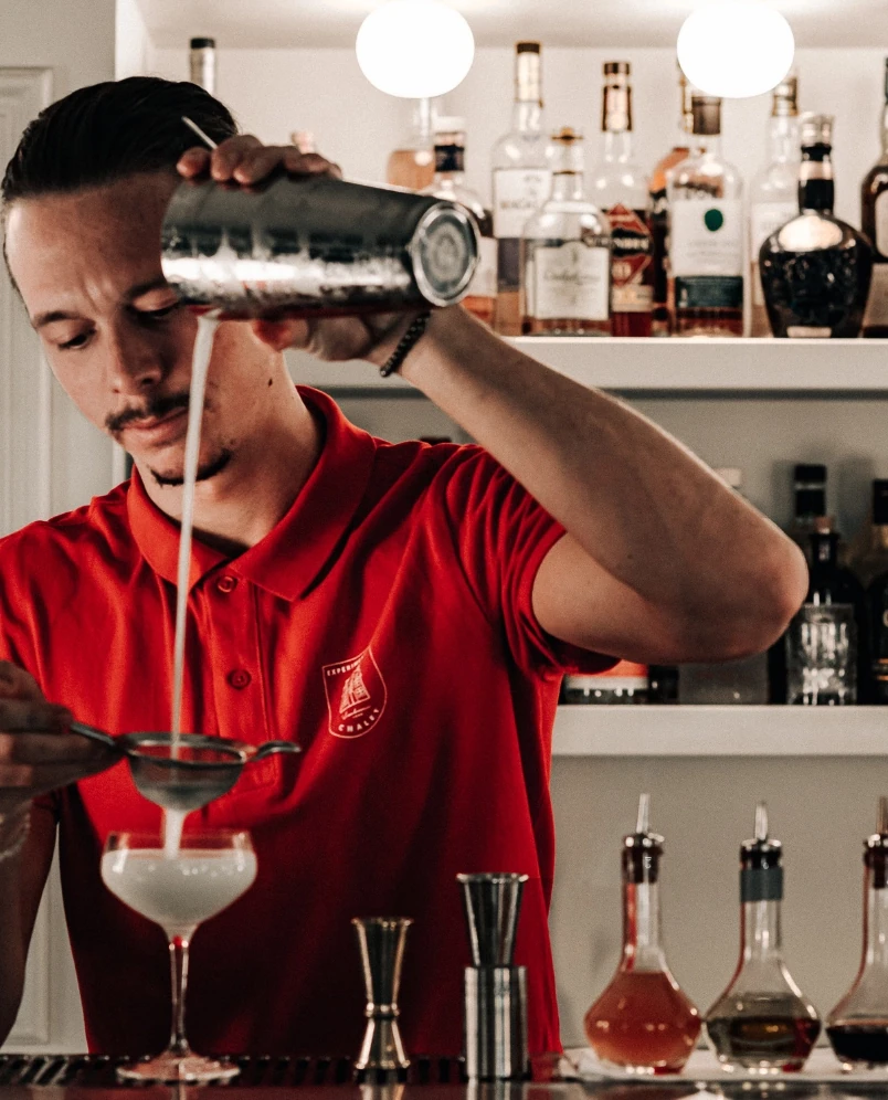 Barista in camicia rossa che versa il cocktail attraverso un colino in un bicchiere di un bar.